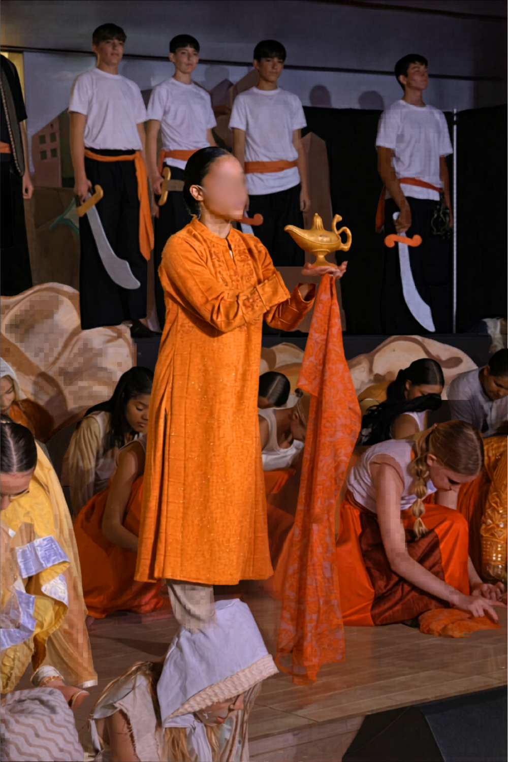 Opening scene of Aladdin Jr with ensemble performer holding the magic lamp, surrounded by cast in Agrabah costumes during a school musical performance.