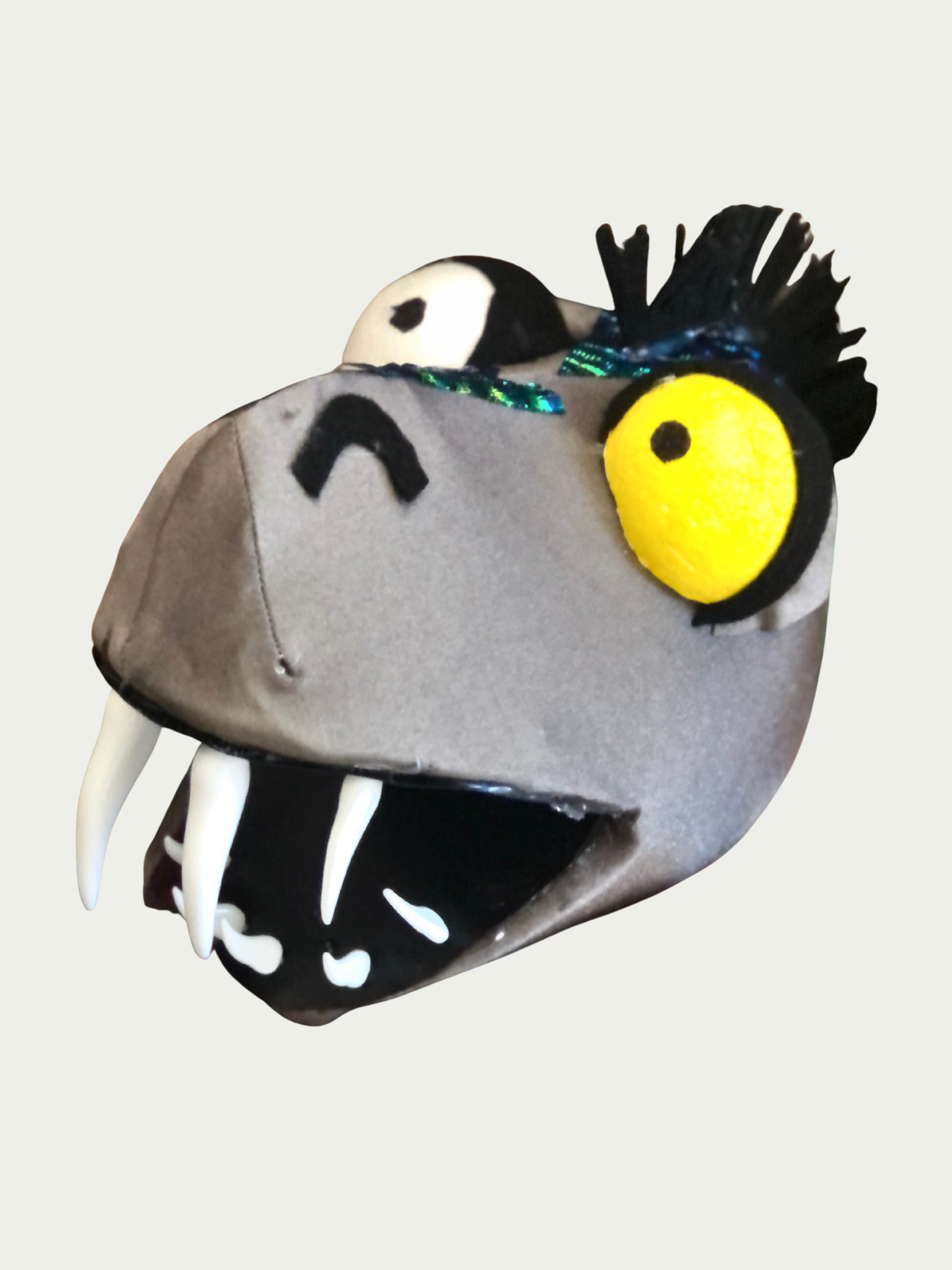Handmade eel puppet head for a youth theater production, sewn from an Etsy pattern with Amazon-purchased teeth and a lightweight styrofoam eye to create a durable. including large yellow eyes, sharp white teeth, black spiky hair, and a gray face.