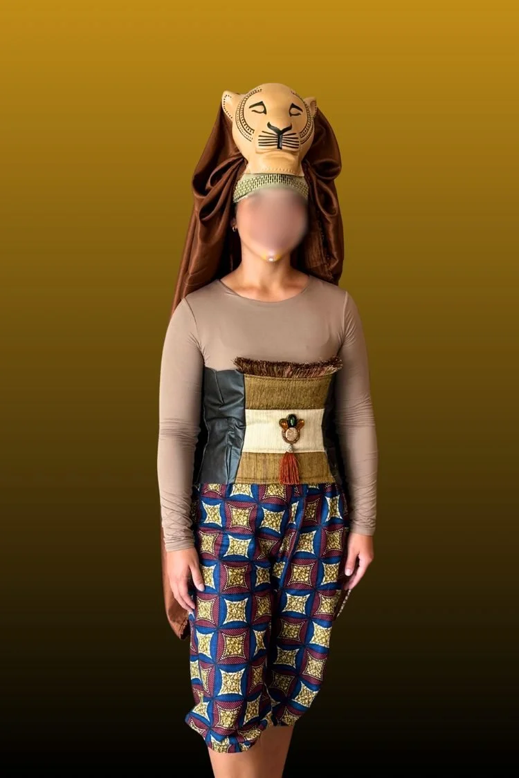 Performer wearing a large lion headpiece, beige long-sleeve top, and colorful patterned pants against a golden background, showcasing a handmade theatrical lion costume.