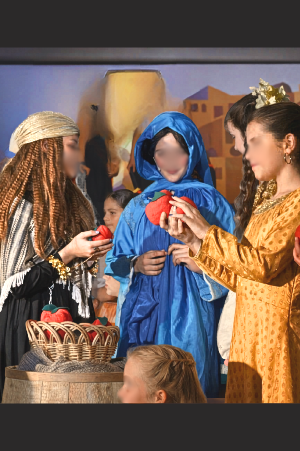 Princess Jasmine in disguise at the Agrabah market in Aladdin Jr, wearing blue cloak while interacting with townspeople during a school musical scene.