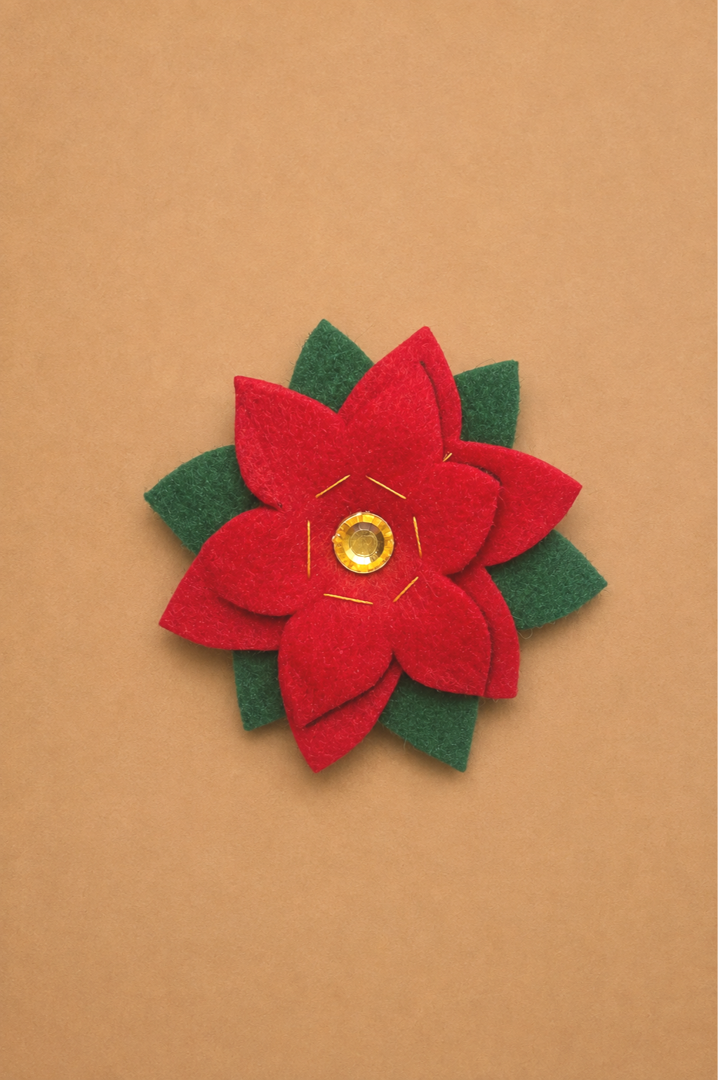 Handmade red and green felt poinsettia brooch with a gold gem center, designed as a DIY holiday accent for an Elf Jr. the Musical costume collar or waistband. An easy no-sew embellishment that adds old-world Christmas charm to school theater costume
