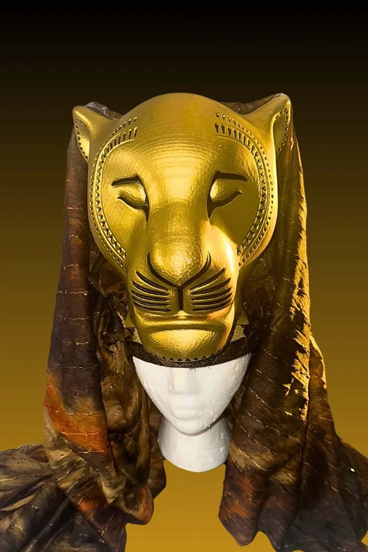 Metallic gold lion face mask with sculpted features and a textured mane, displayed against a rustic background for a Lion King JR. stage costume.