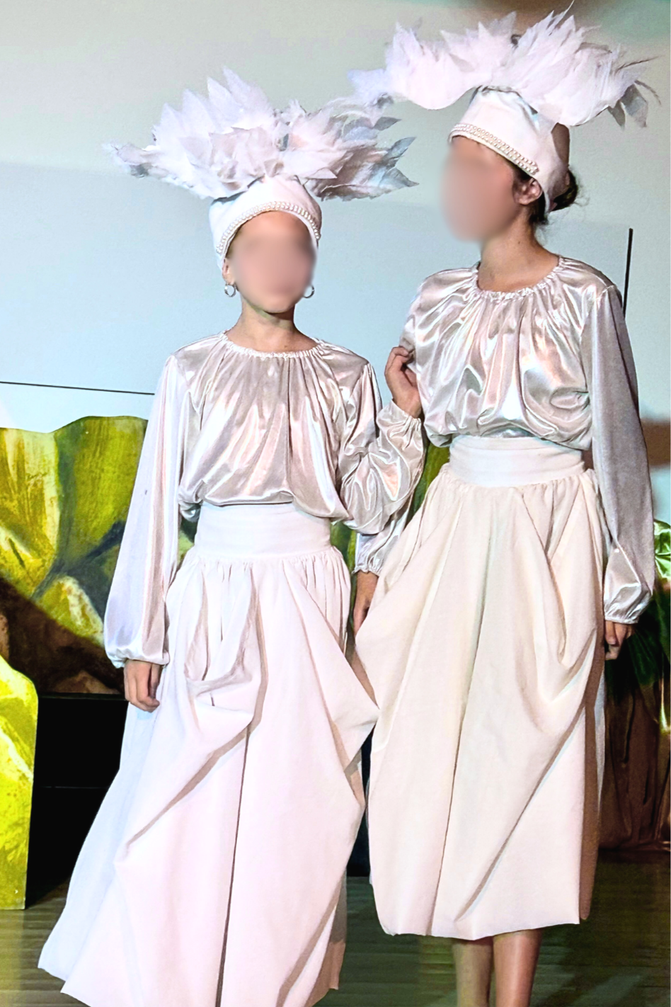Two youth theater performers wear white bird ensemble costumes with satin silver blouses and DIY sheer drape skirts that are budget-friendly and easy to sew in under an hour for school musical ensembles. Feather headpiece made of EVA foam.