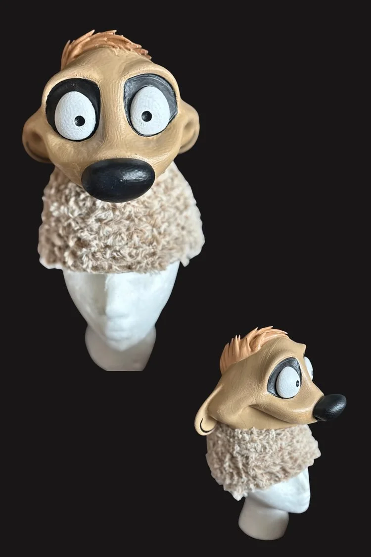 Two views of a handmade animal costume headpiece featuring oversized blue eyes, a black nose, tan facial details, and textured faux fur, displayed against a black background.