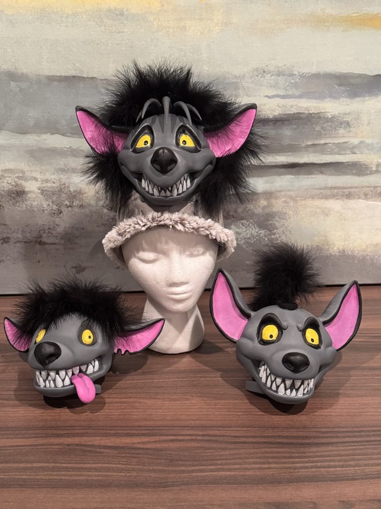 Lion King JR. Hyena Masks: Three handmade hyena costume headpieces featuring gray faces, large pink ears, yellow eyes, black faux fur, and exaggerated expressions for The Lion King JR.