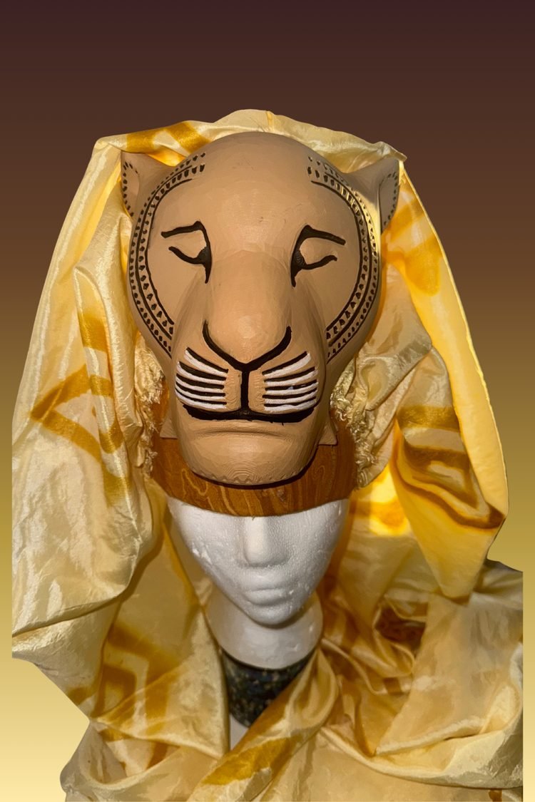 Decorative lion costume mask with a tan face, dark facial outlines, and a golden mane, paired with gold fabric for a Lion King JR. theatrical costume.