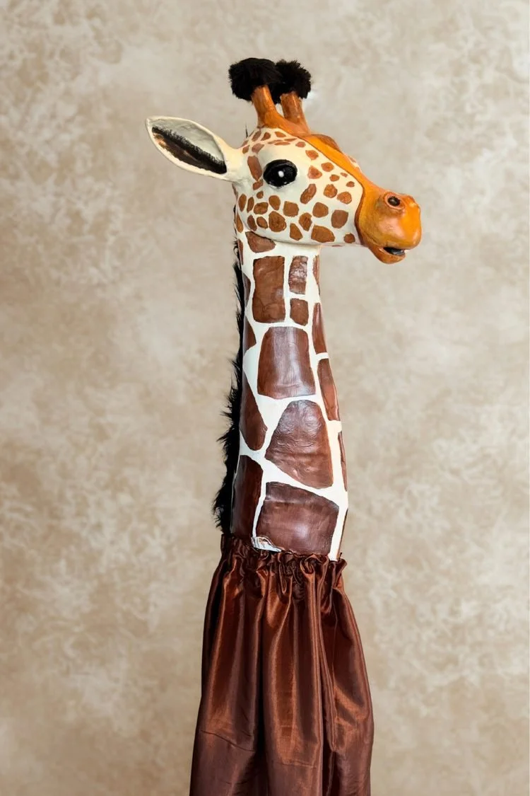 Handmade giraffe puppet costume featuring a long patterned neck, sculpted giraffe head, and brown fabric body, designed for a school theater production of The Lion King JR.