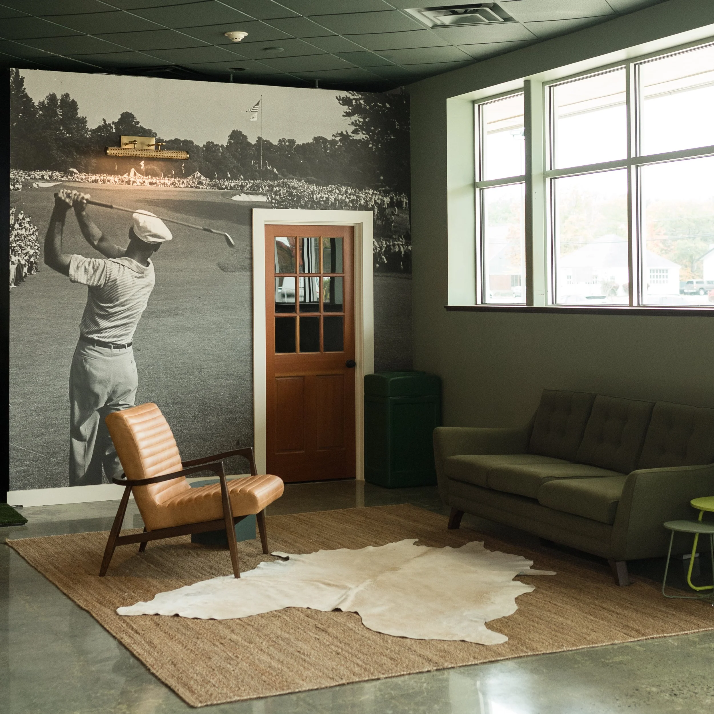 Golf club lounge with vintage golfer mural, cognac leather chair, olive sofa and cowhide rug at Coachclub in Hampton, NH by Ivory & Bone Interiors