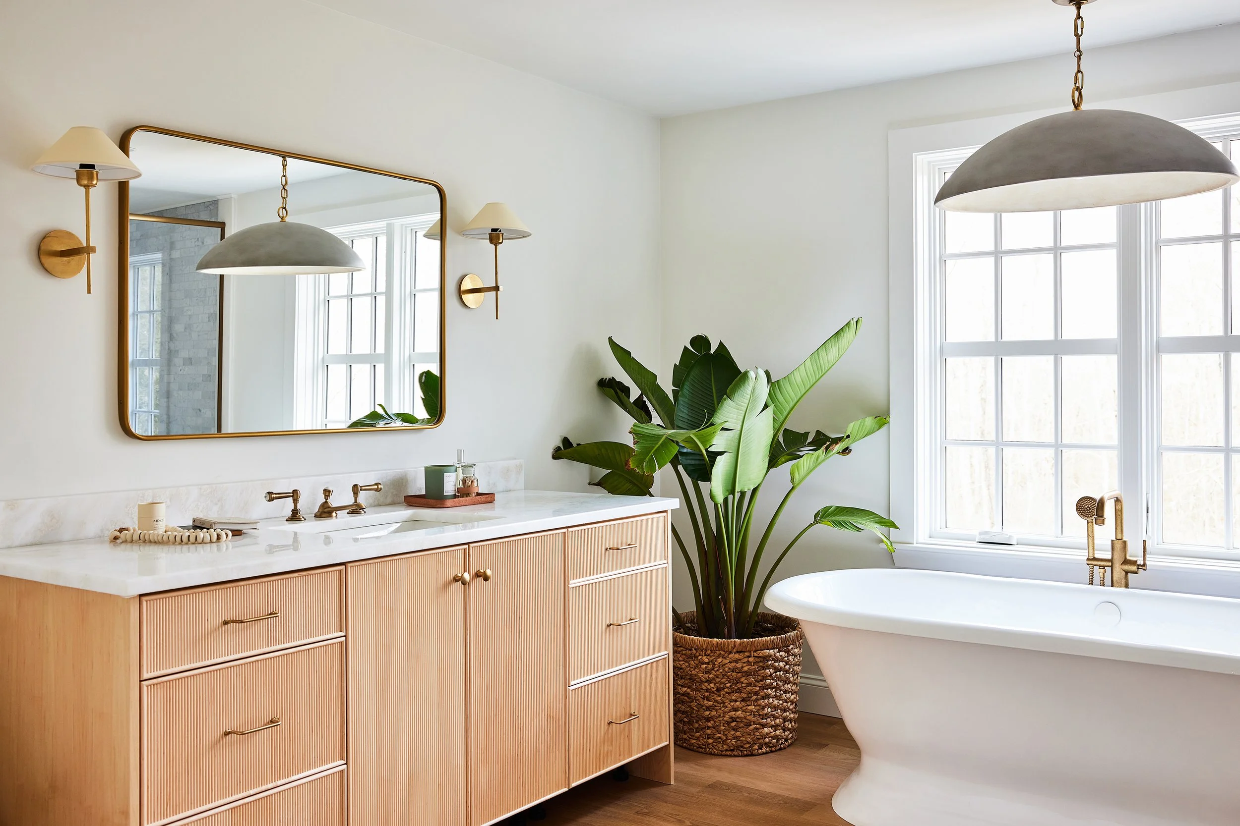 Primary bath with a fluted oak vanity, brass mirror and soaking tub in a Rye, NH home by Ivory & Bone Interiors
