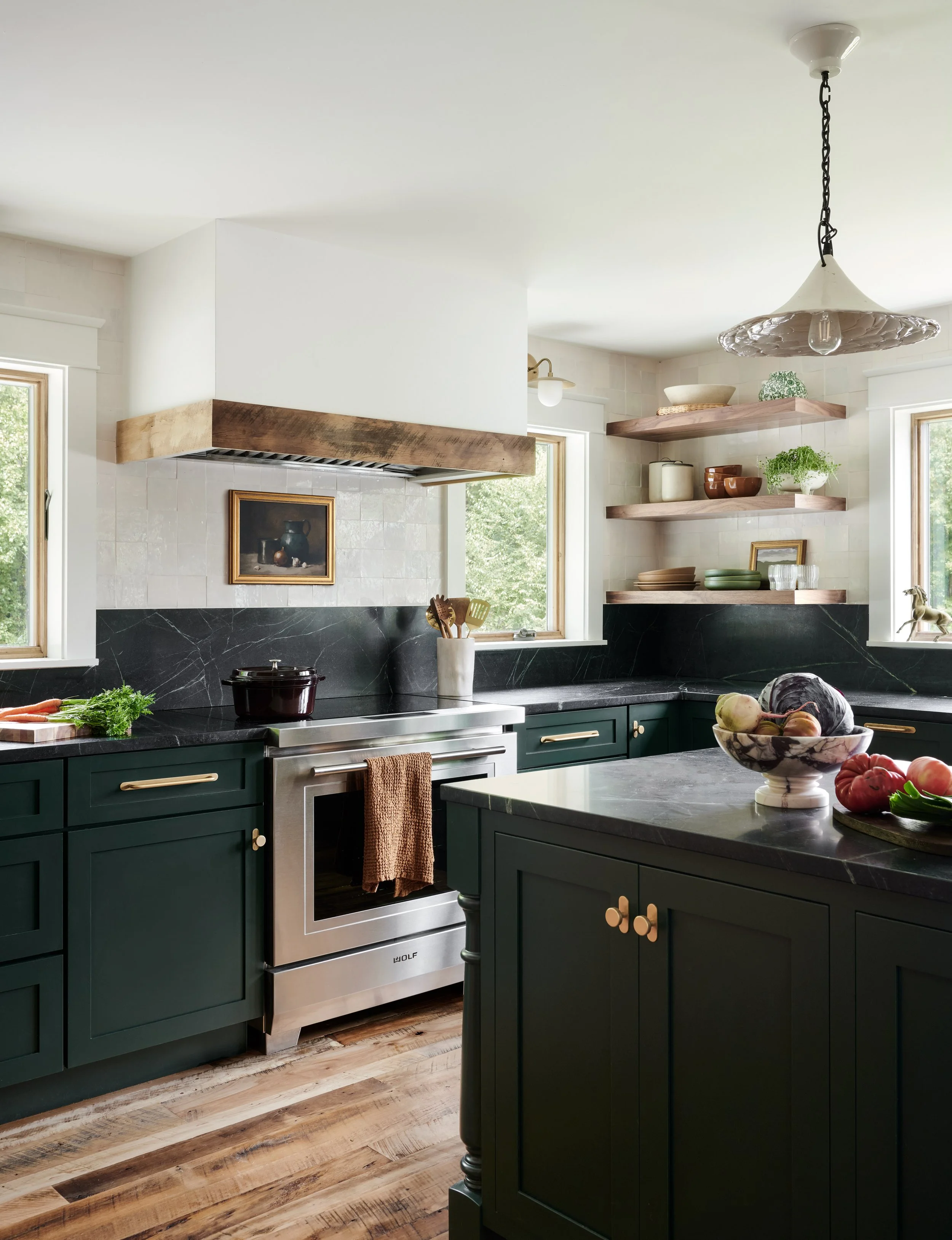 Forest green kitchen with black stone counters, brass hardware, timber beam range hood and open shelving in a Groveland, MA home by Ivory & Bone Interiors