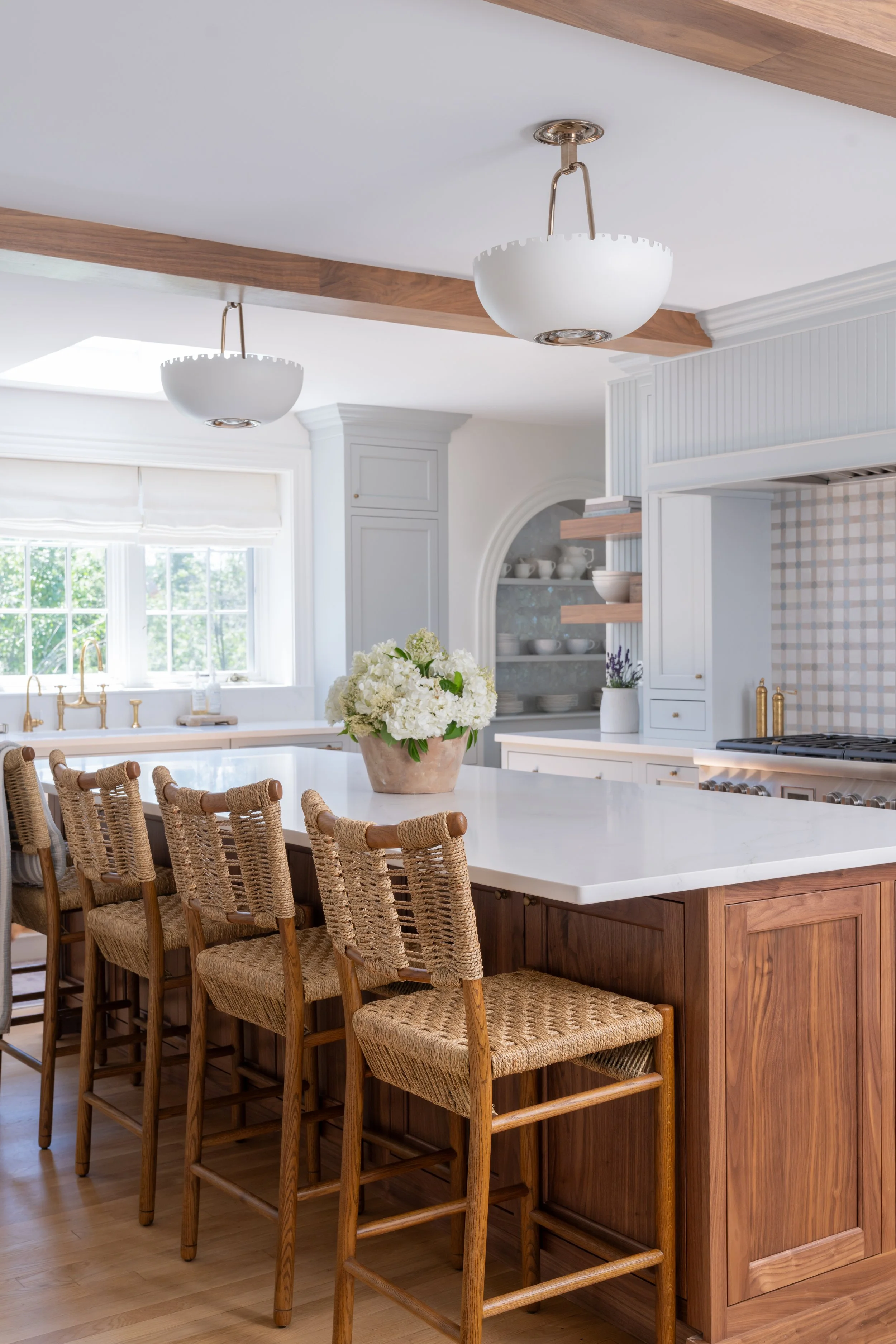 White kitchen with walnut island, woven counter stools, exposed wood beam and arched open shelving at Old Farm Way, designed by Ivory & Bone Interiors