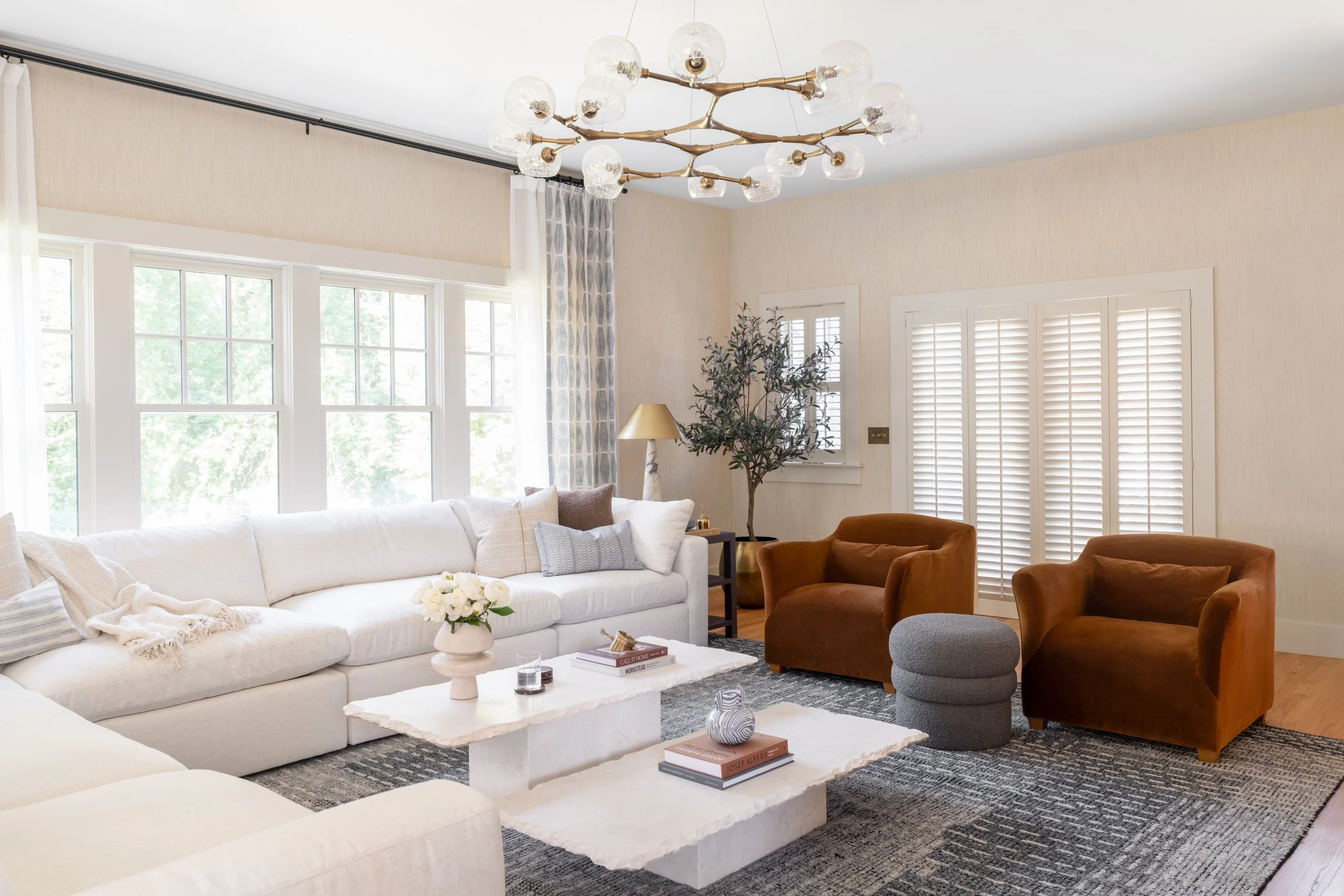 Light-filled living room with a brass chandelier and cognac velvet chairs in an Amesbury, MA home by Ivory & Bone Interiors