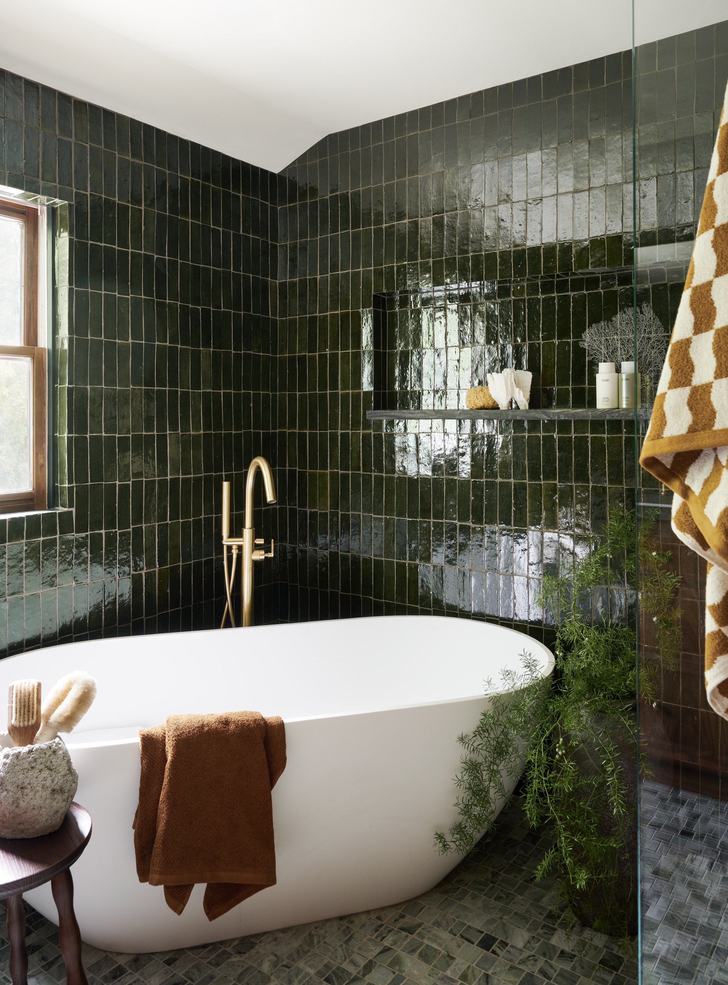 Freestanding soaking tub in a deep green tiled primary bathroom with brass fixtures by Ivory & Bone Interiors, Groveland, MA