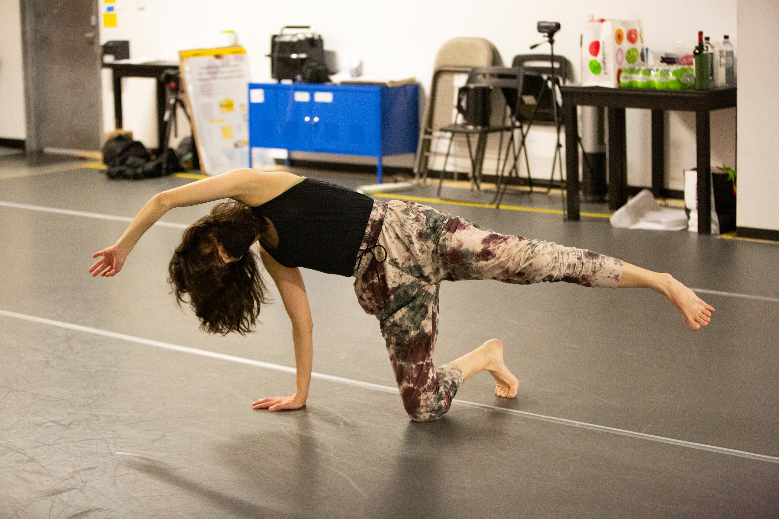 A white woman practicing a dance pose. They are sideways, supported by one knee and one hand with the other leg and arm outstretched.