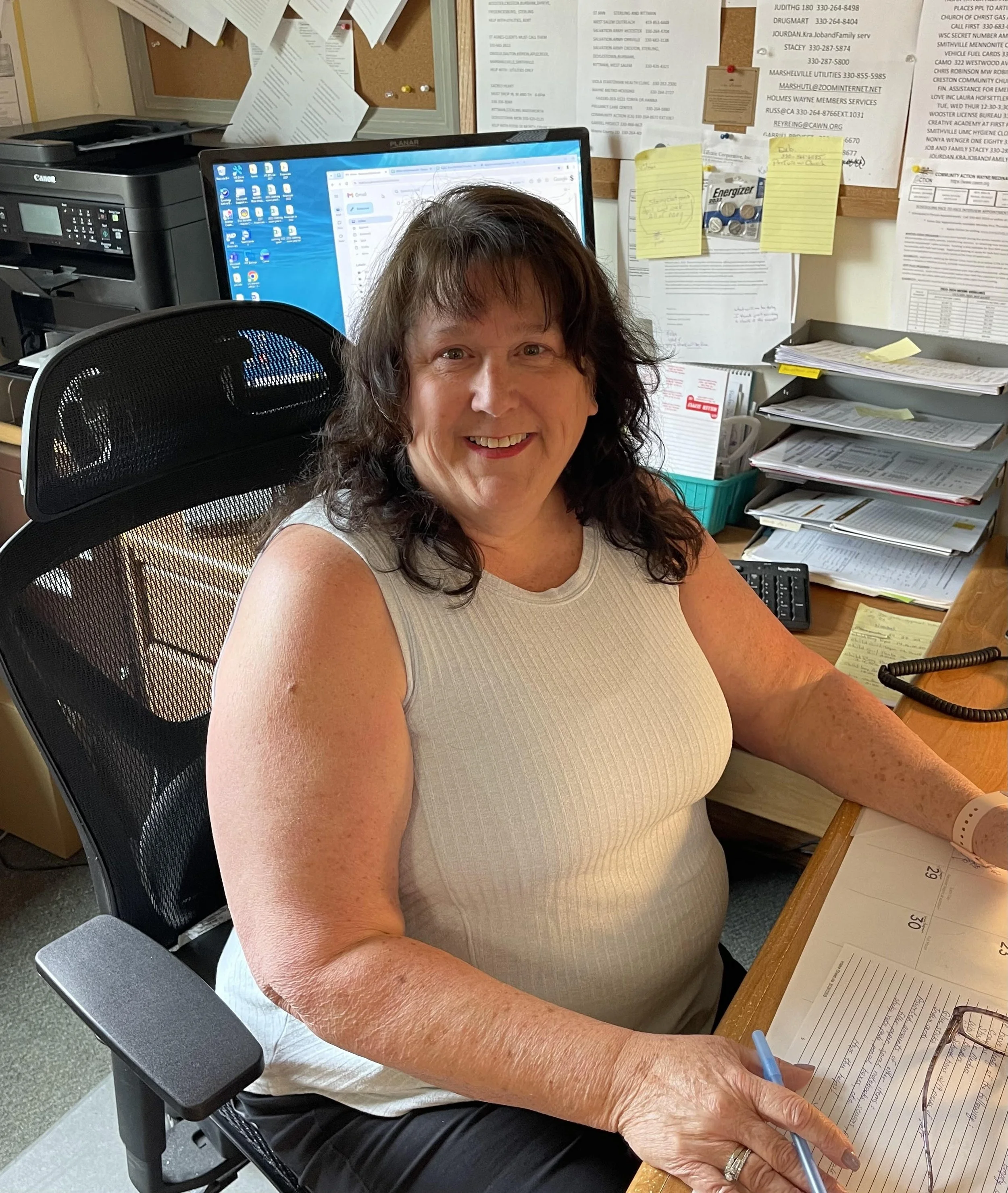 A white, two-story house with burgundy trim and a small front porch, surrounded by autumn trees with fallen leaves on the ground.