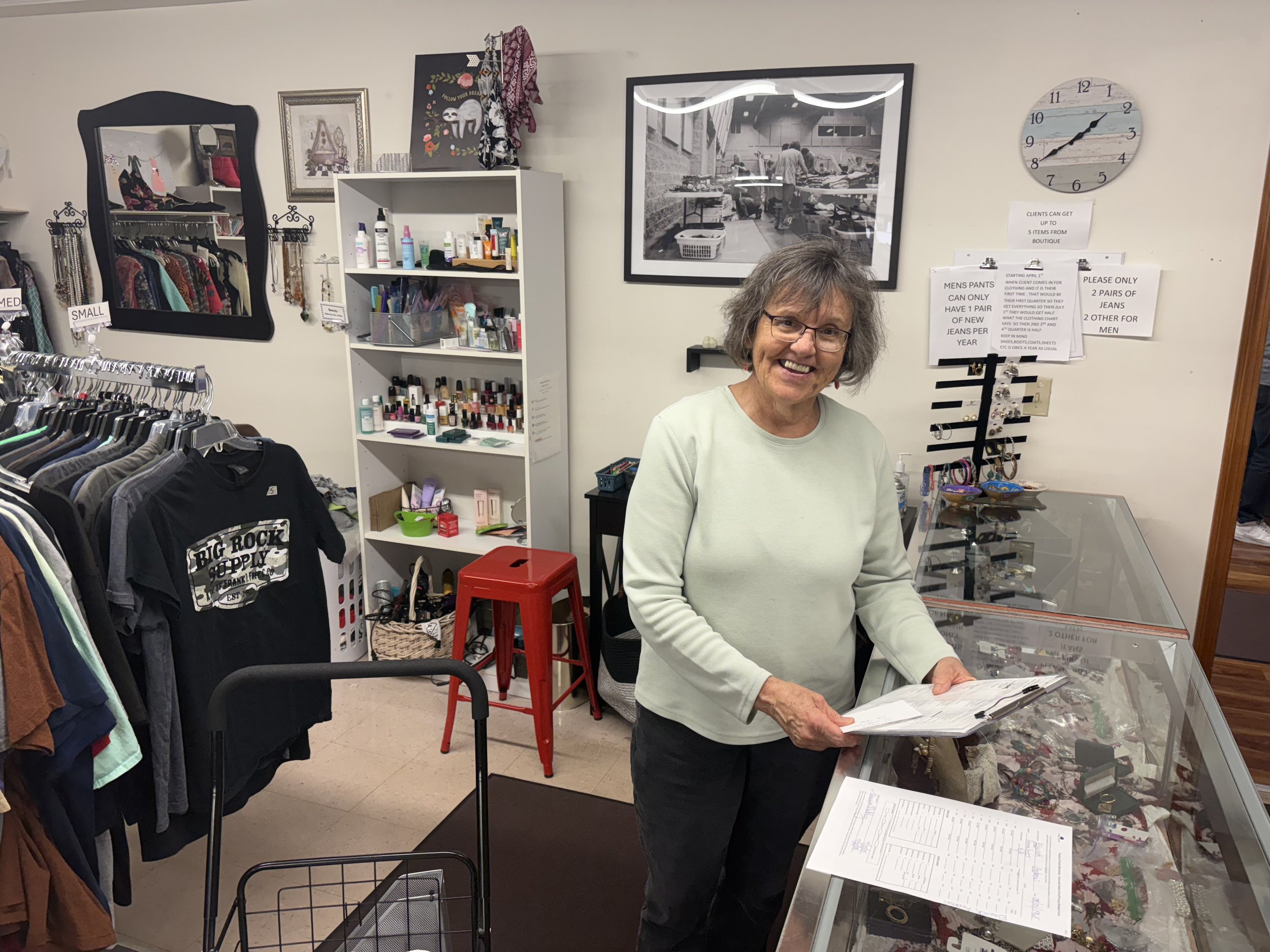 Person folding a stack of folded clothes on the floor, including jeans, t-shirts, and other garments.