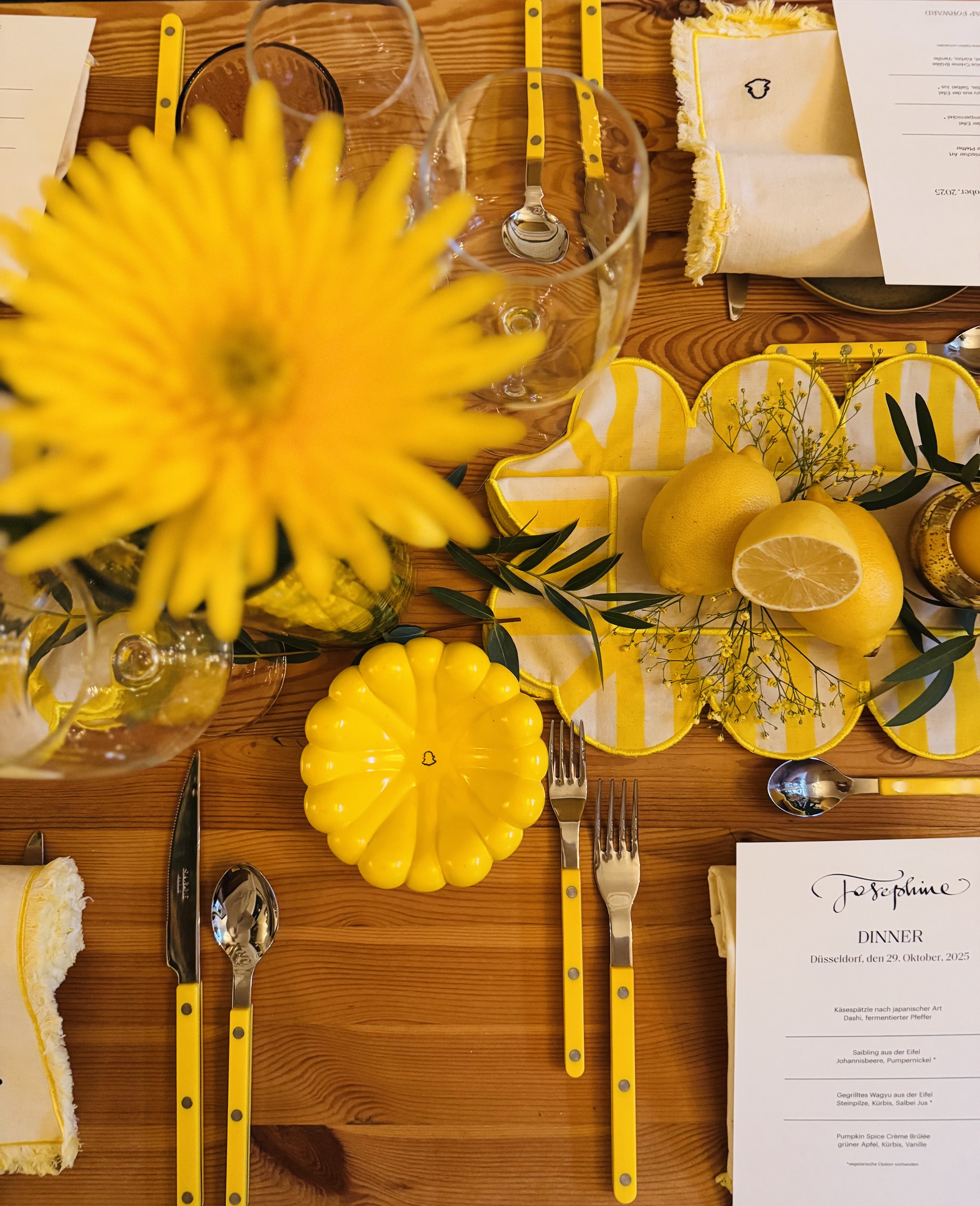 Ein gedeckter Tisch mit gelben Dekorationen, Zitronen, Blumen und Besteck, passend für ein Abendessen.
