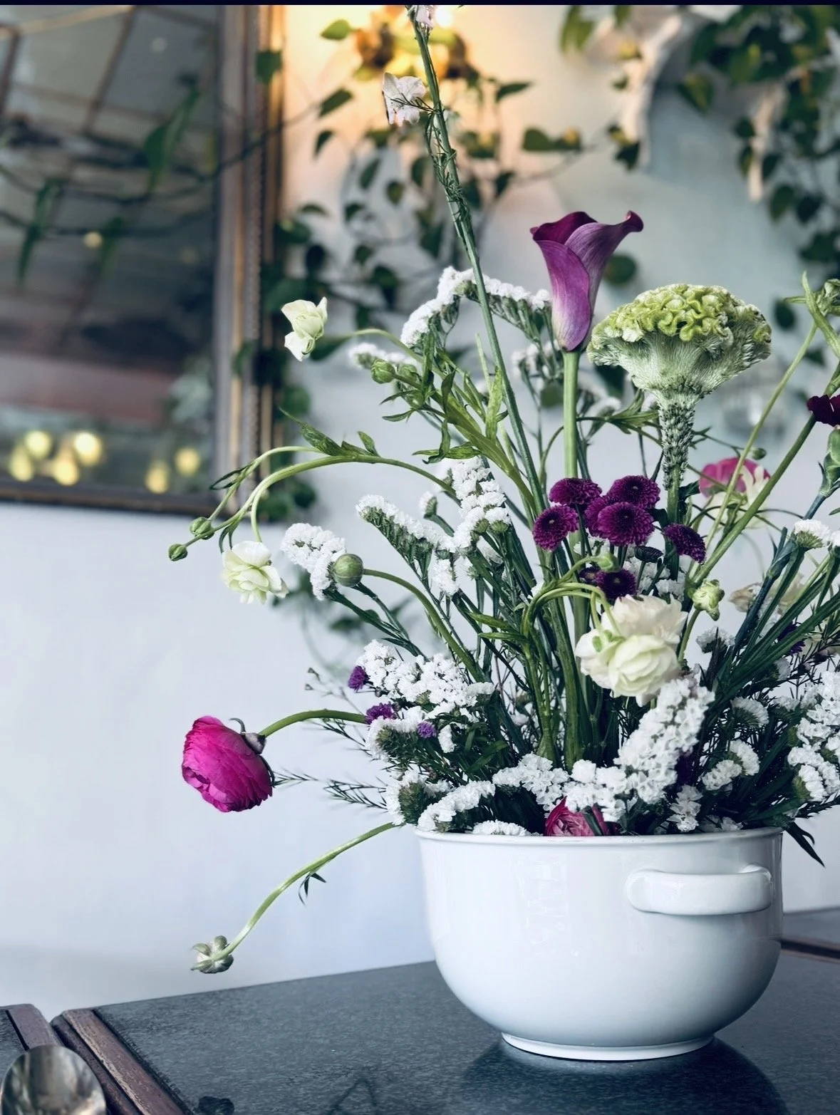 Blumenstrauß in weißer Schüssel mit verschiedenen bunten Blumen und Gräsern, auf schwarzem Tisch