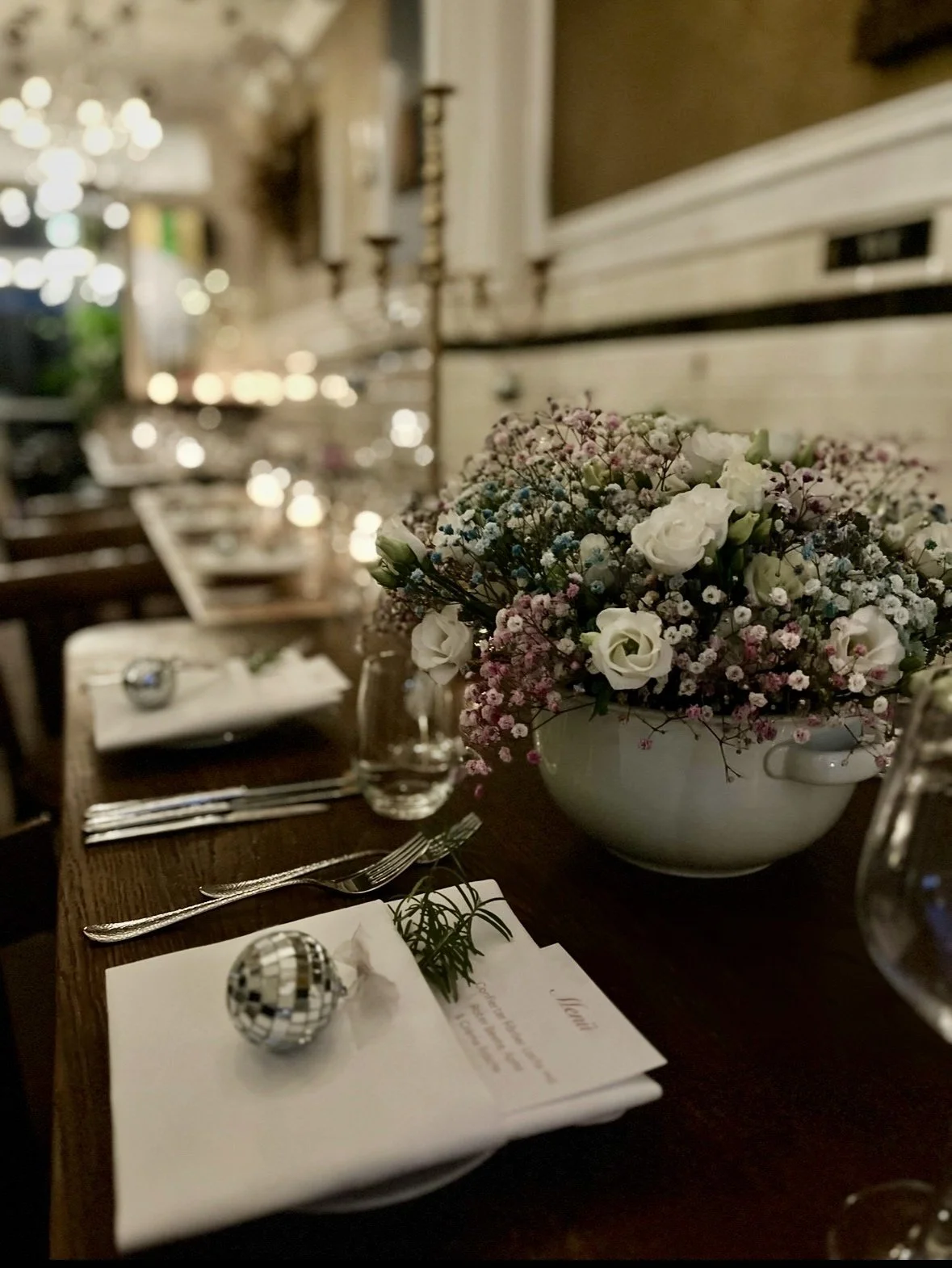 Elegant gedeckter Tisch mit Sonnenblumenstrauß, Silberkugel, Weingläser, Besteck und Menükarte in einem festlichen Restaurant.