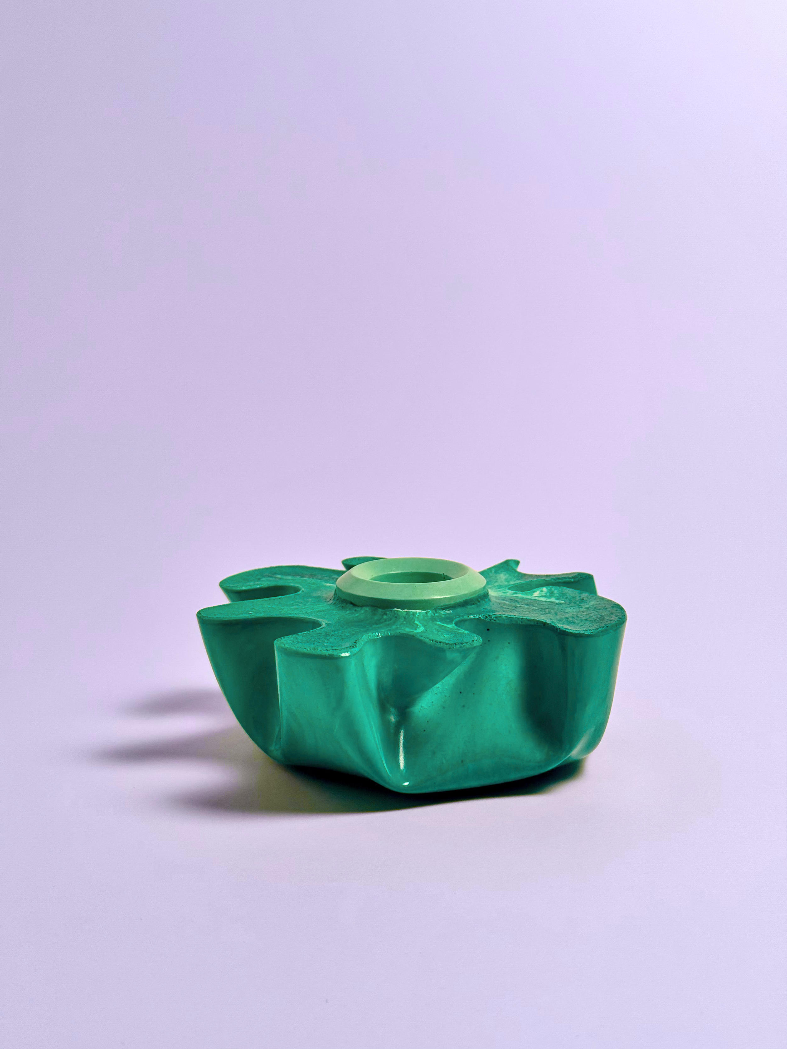 Eine grüne, abstrakte Skulptur in Form einer Blume auf einem hellen Hintergrund.