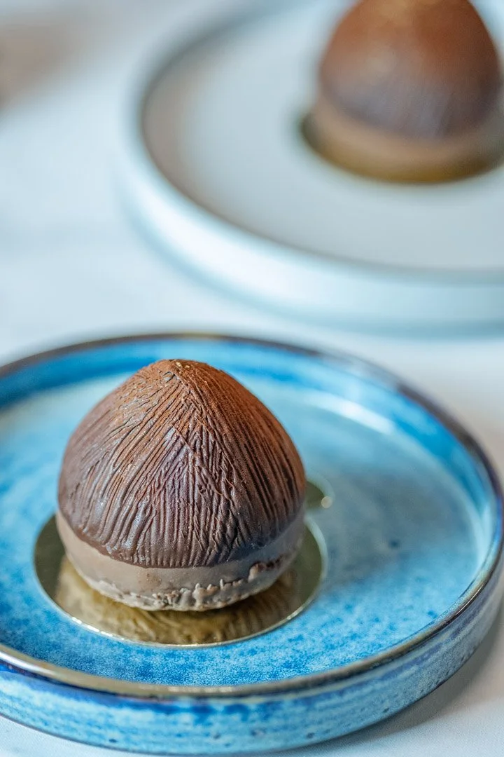 Two toasted marshmallows with a chocolate coating, sitting on a black tray on a wooden surface.