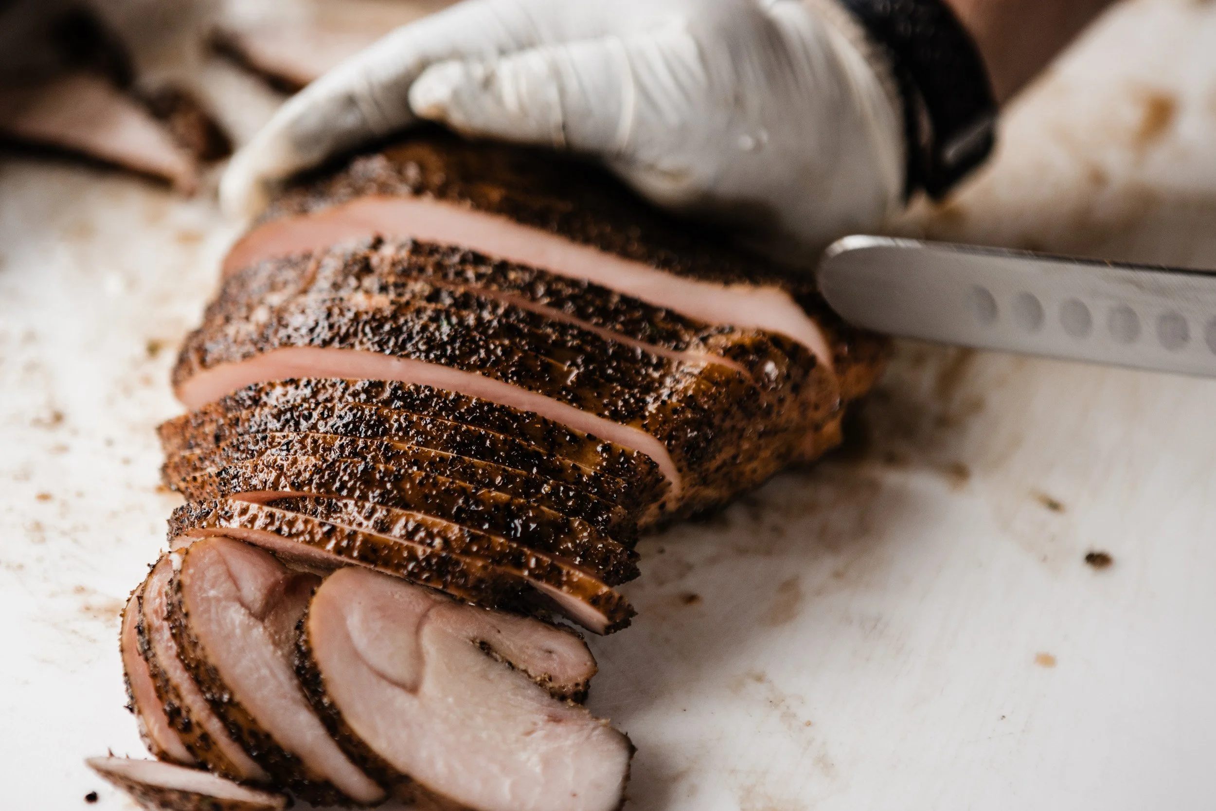 Close-up of gloved chef slicing perfectly smoked turkey breast on a white cutting board.