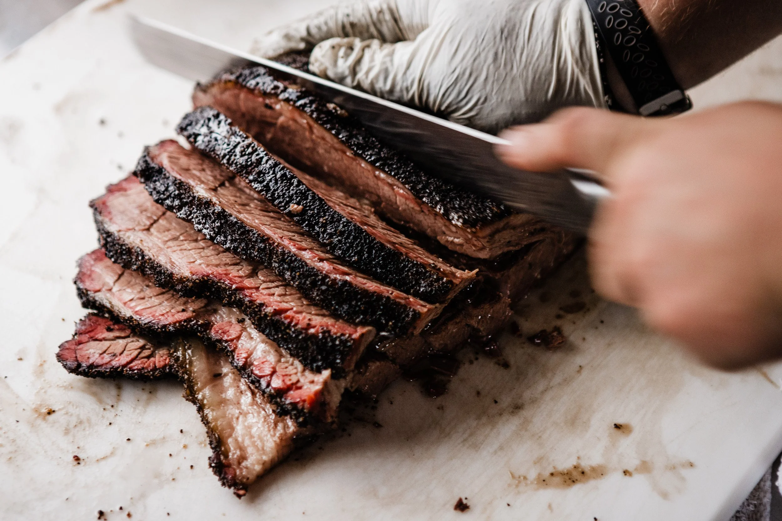 Sliced cooked brisket on butcher paper, with a person cutting it with a knife.