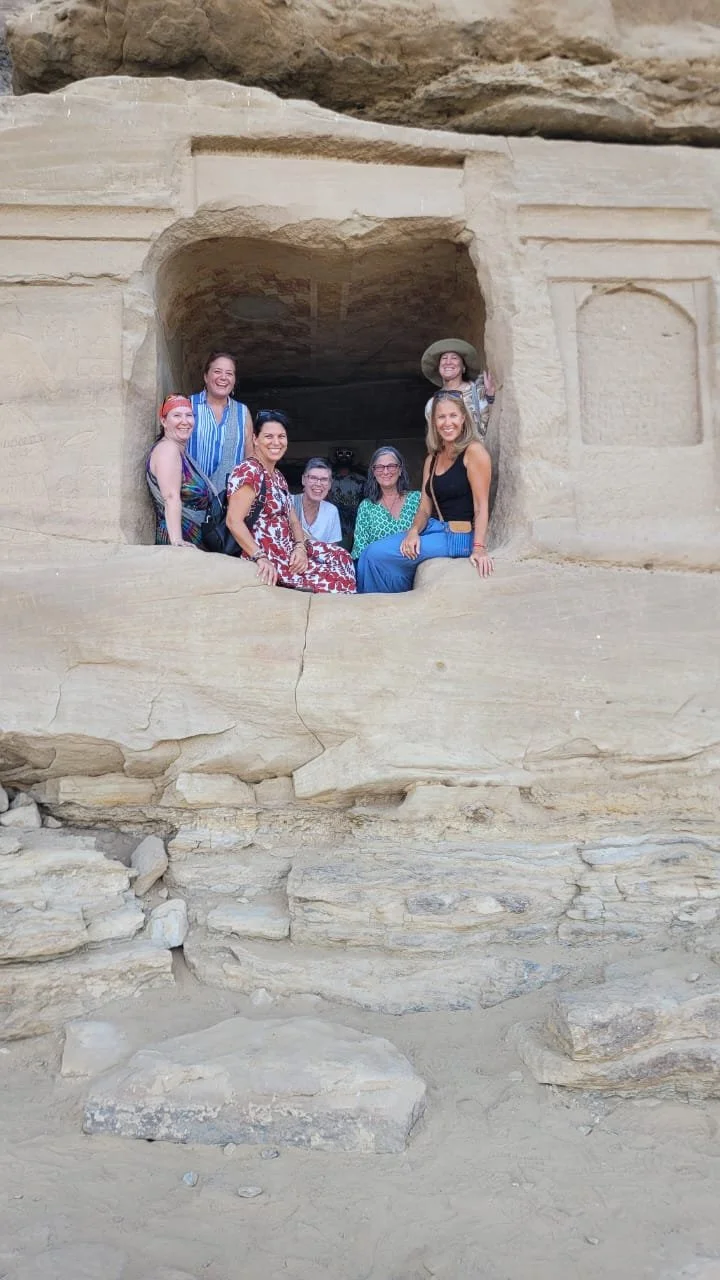Group of seven women posing and smiling inside a large ancient stone structure with carved openings.
