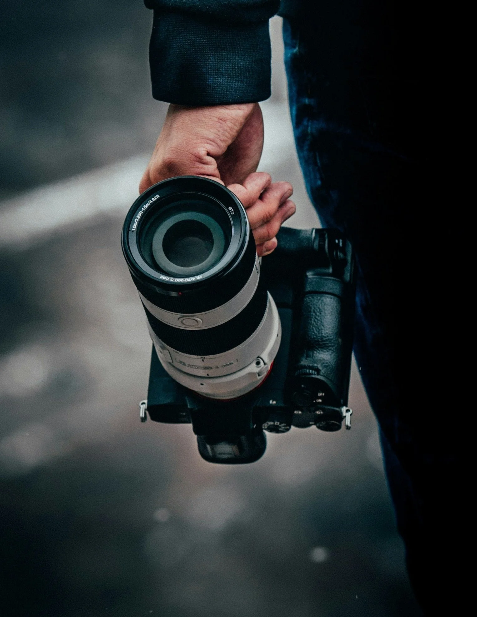 Person holding a professional camera with a large telephoto lens in their right hand.