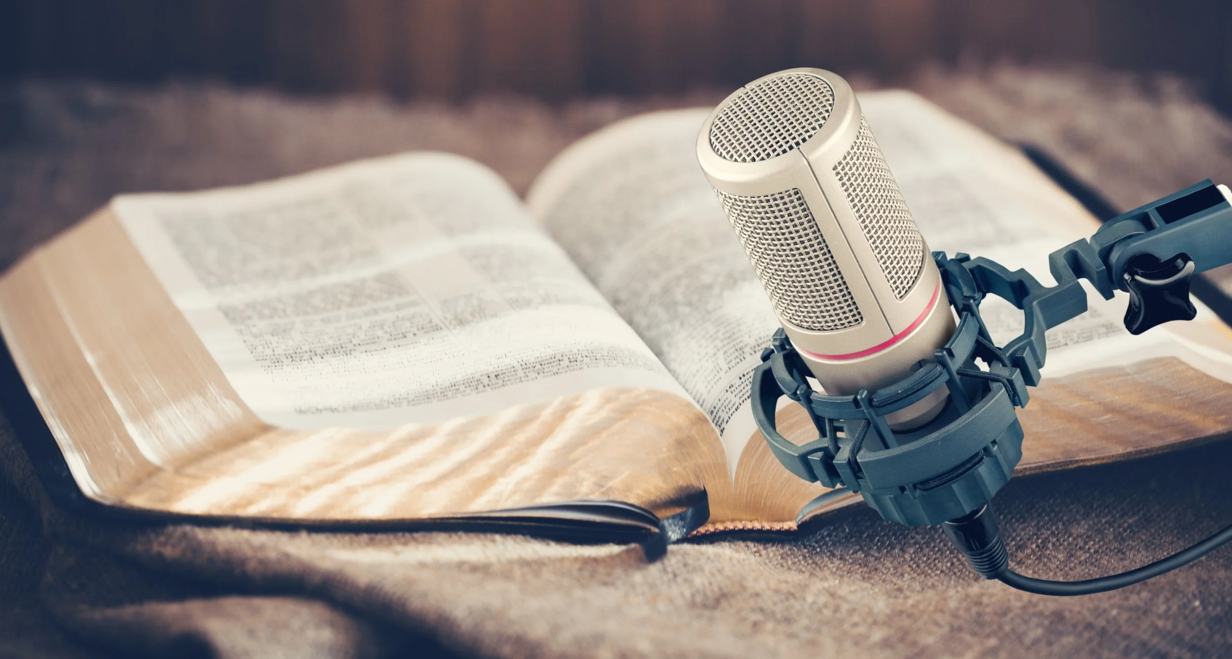 Open Bible with a microphone placed on a stand in front of it, set on a brown textured surface.
