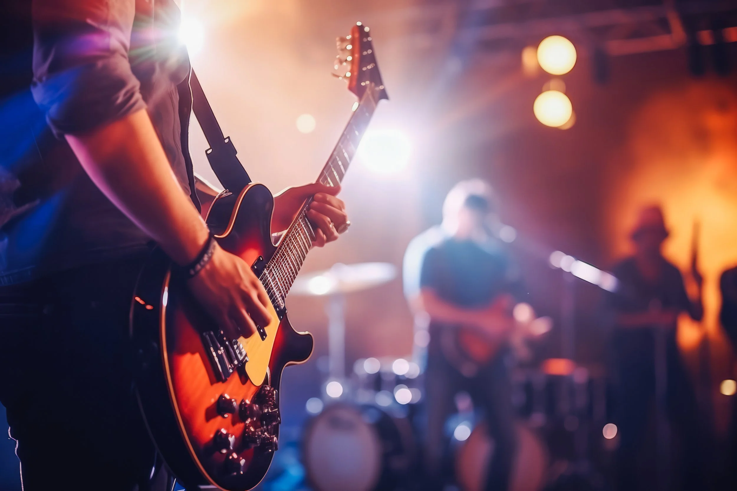 A musician playing an electric guitar on stage with colorful stage lights and a band in the background.
