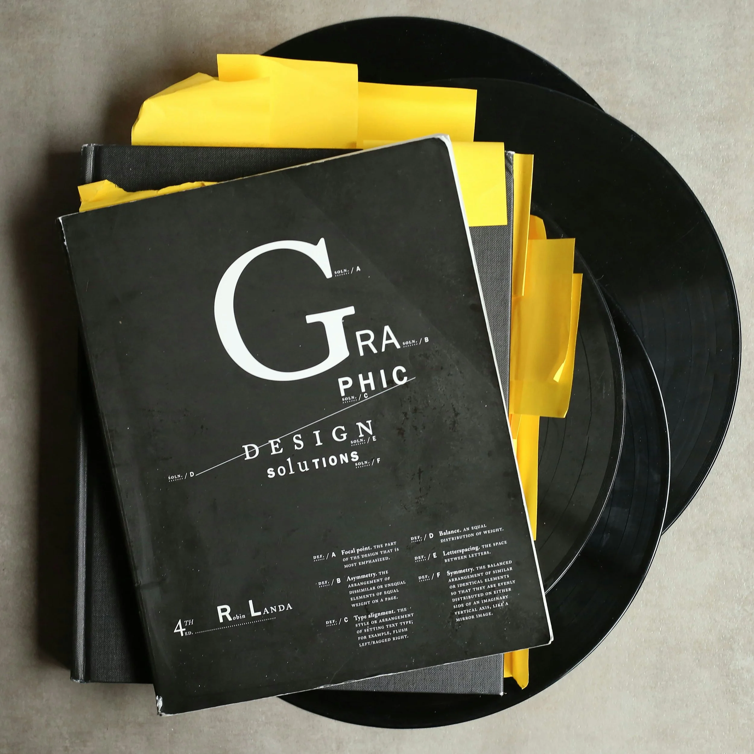 A black book titled "Graphic Design Solutions" with yellow sticky notes placed on top of it, resting on a black circular record.