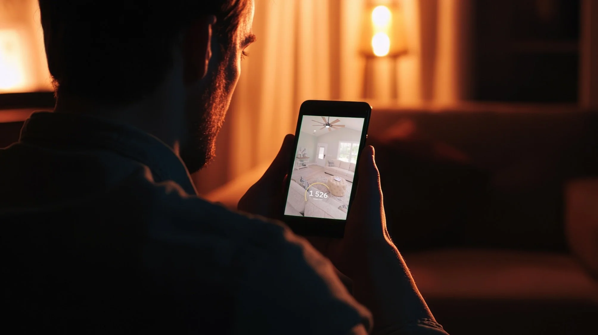 A man taking a photo of a living room with a smartphone in a dimly lit room.