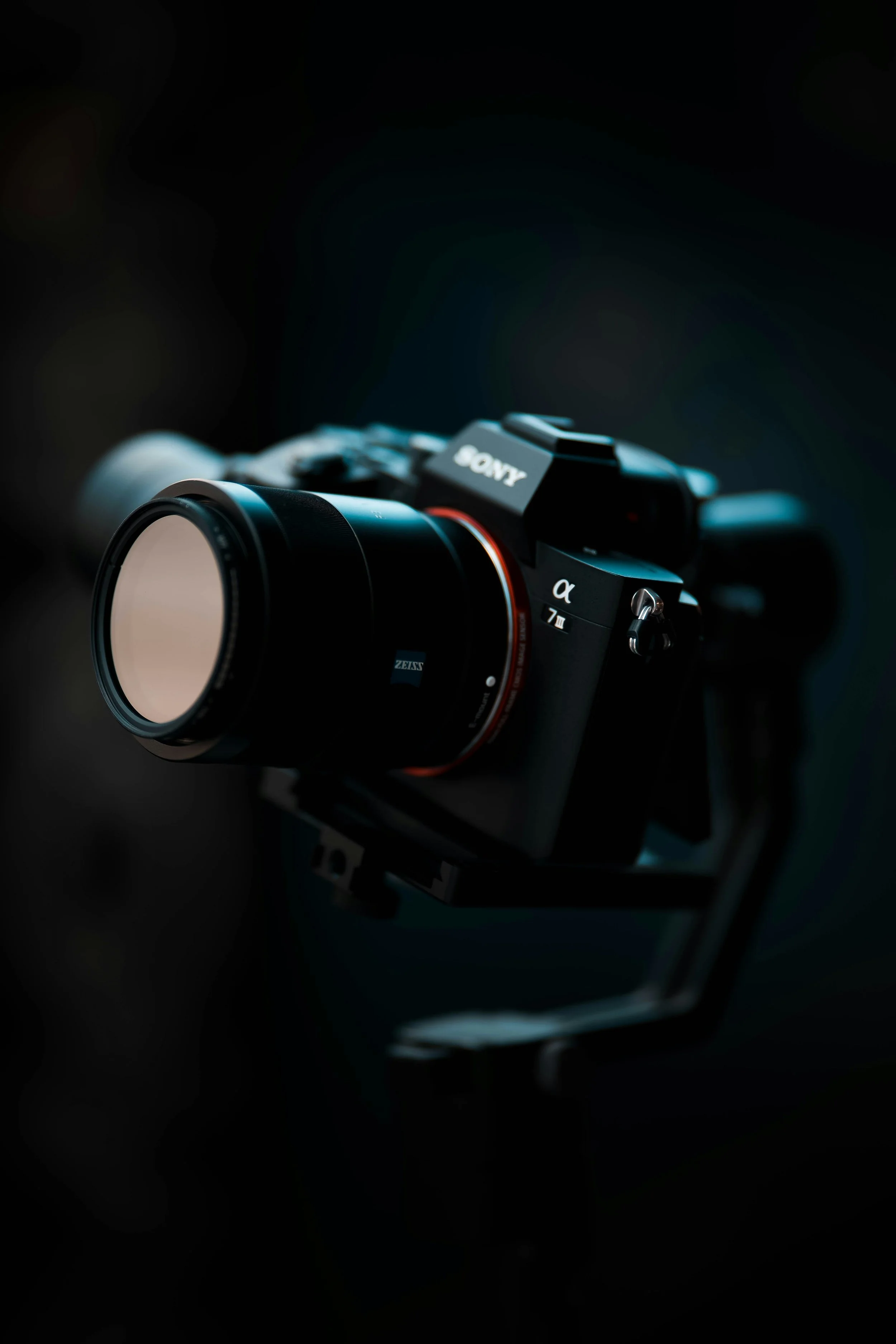 A Sony mirrorless camera with a ZEISS lens mounted on a stabilizer against a dark background.