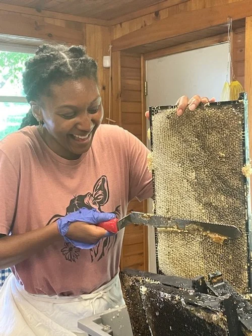 A woman smiling while honeycomb frames with beeswax are removed from a hive.
