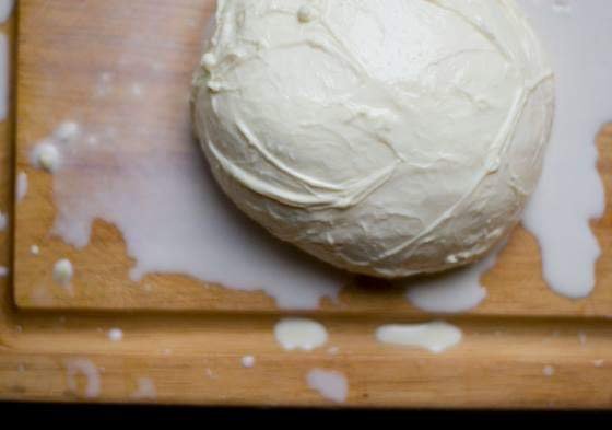A ball of dough on a wooden cutting board with some spilled flour and dough around it.
