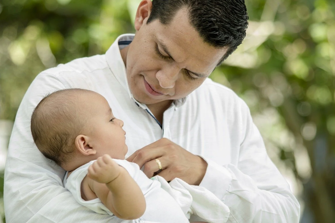 A man holding a baby outdoors, looking at the baby affectionately, representing satisfied clients reunited with their children after successful legal appeals.