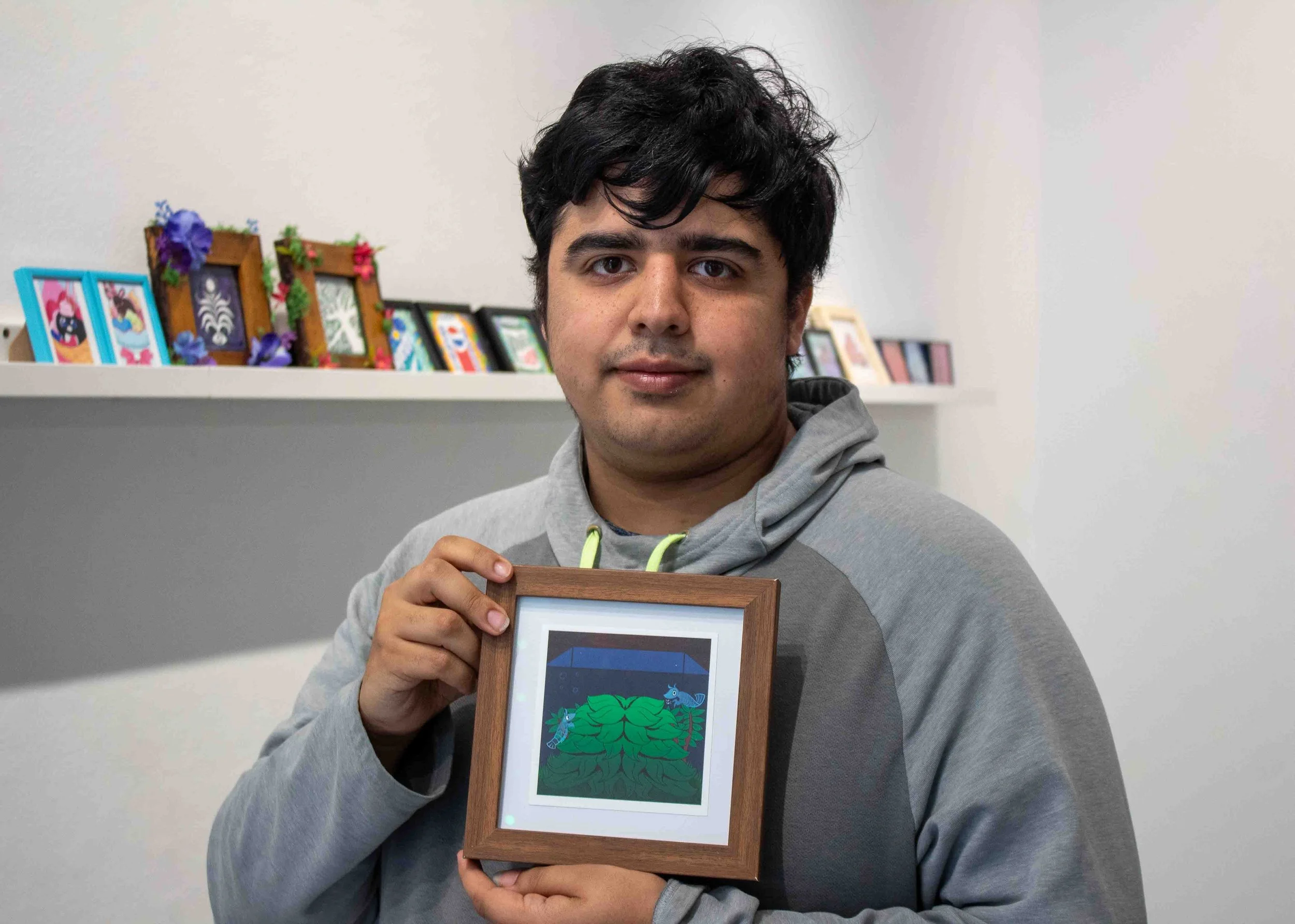 Alumni artist S.A. Arnold stands in the Shop Columbia display titled “MINI MINI: A Showcase of Miniature Works” holding his piece titled, “Tank View” during the artist reception on Thursday, Apr. 9, 2026.  