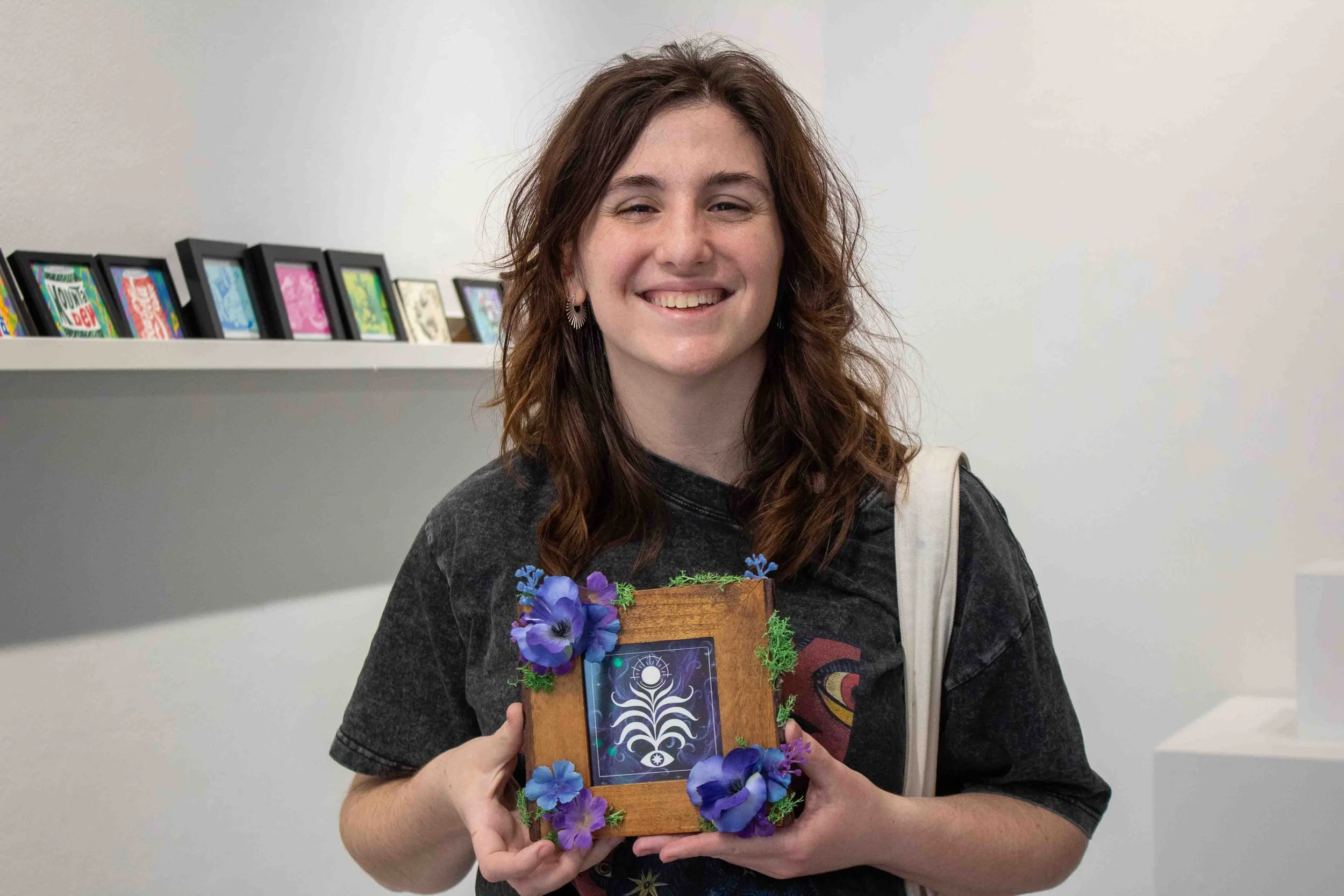 Alumni artist and 2023 Manifest creative director Giovanna Martin stands in the Shop Columbia display titled “MINI MINI: A Showcase of Miniature Works” holding her piece titled, “Blossom” during the artist reception on Thursday, Apr. 9, 2026. 