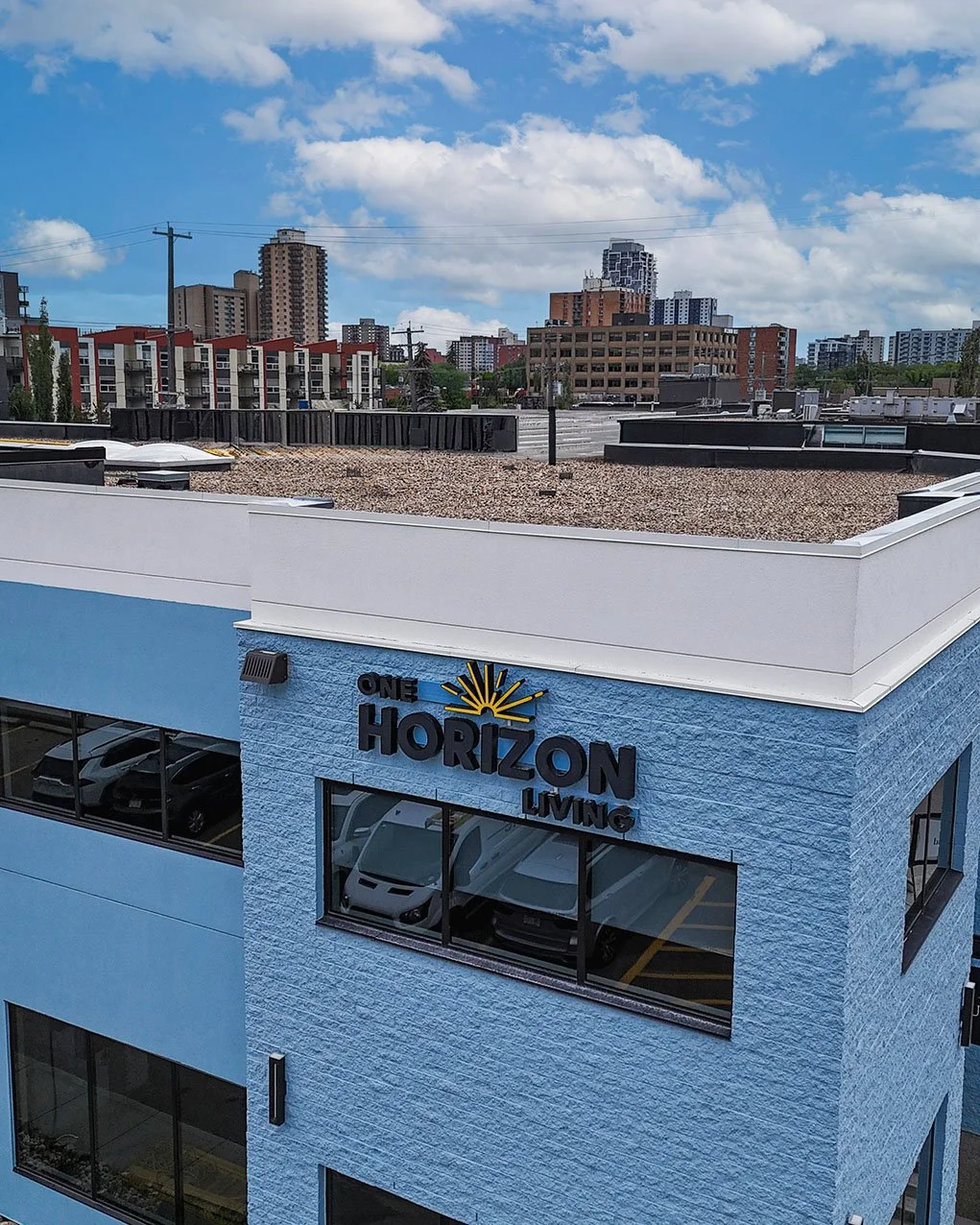 A blue building with a sign that reads 'One Horizon Living' on the upper part, with city buildings and a partly cloudy sky in the background.