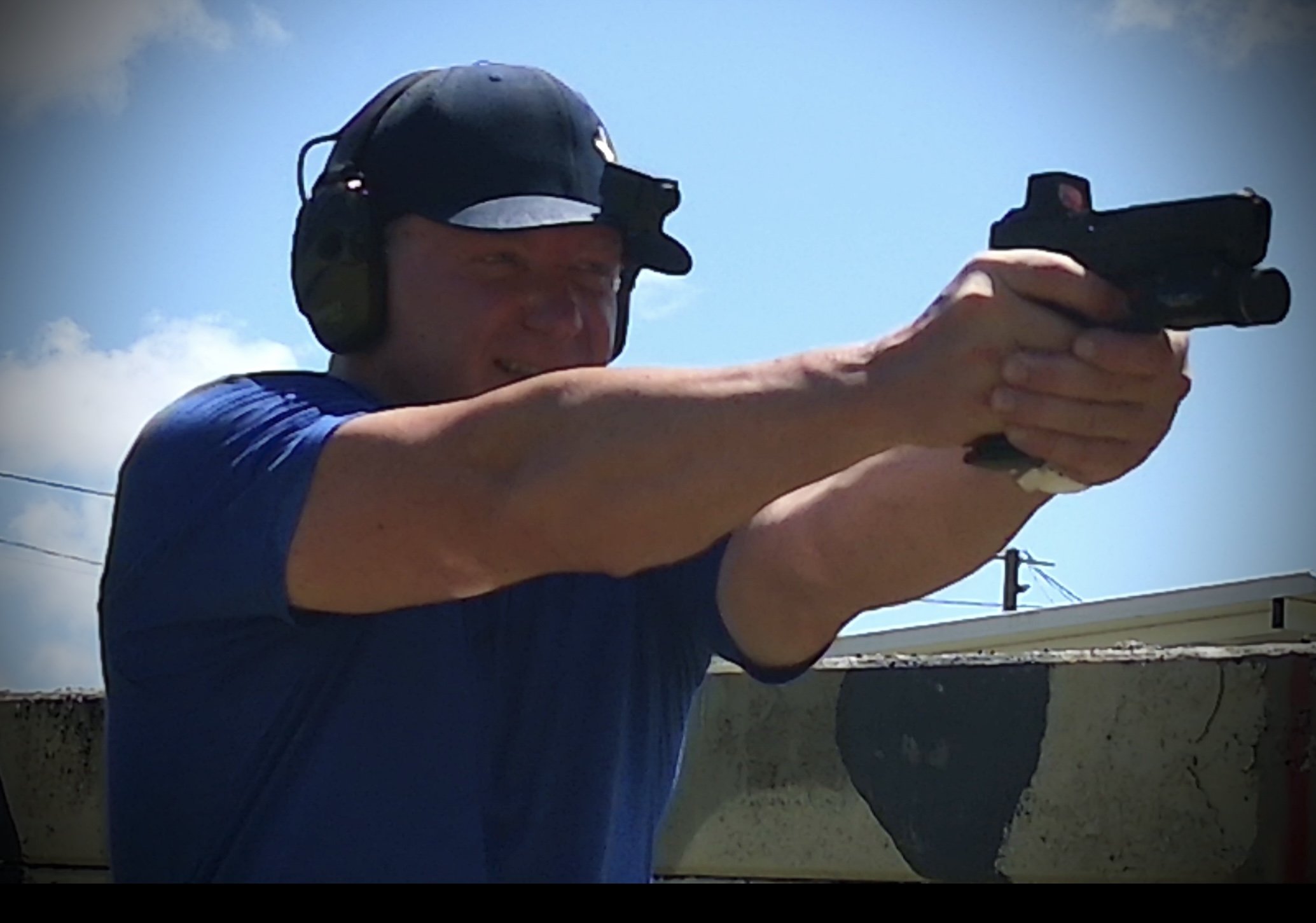 Man shooting a handgun outdoors on a sunny day.