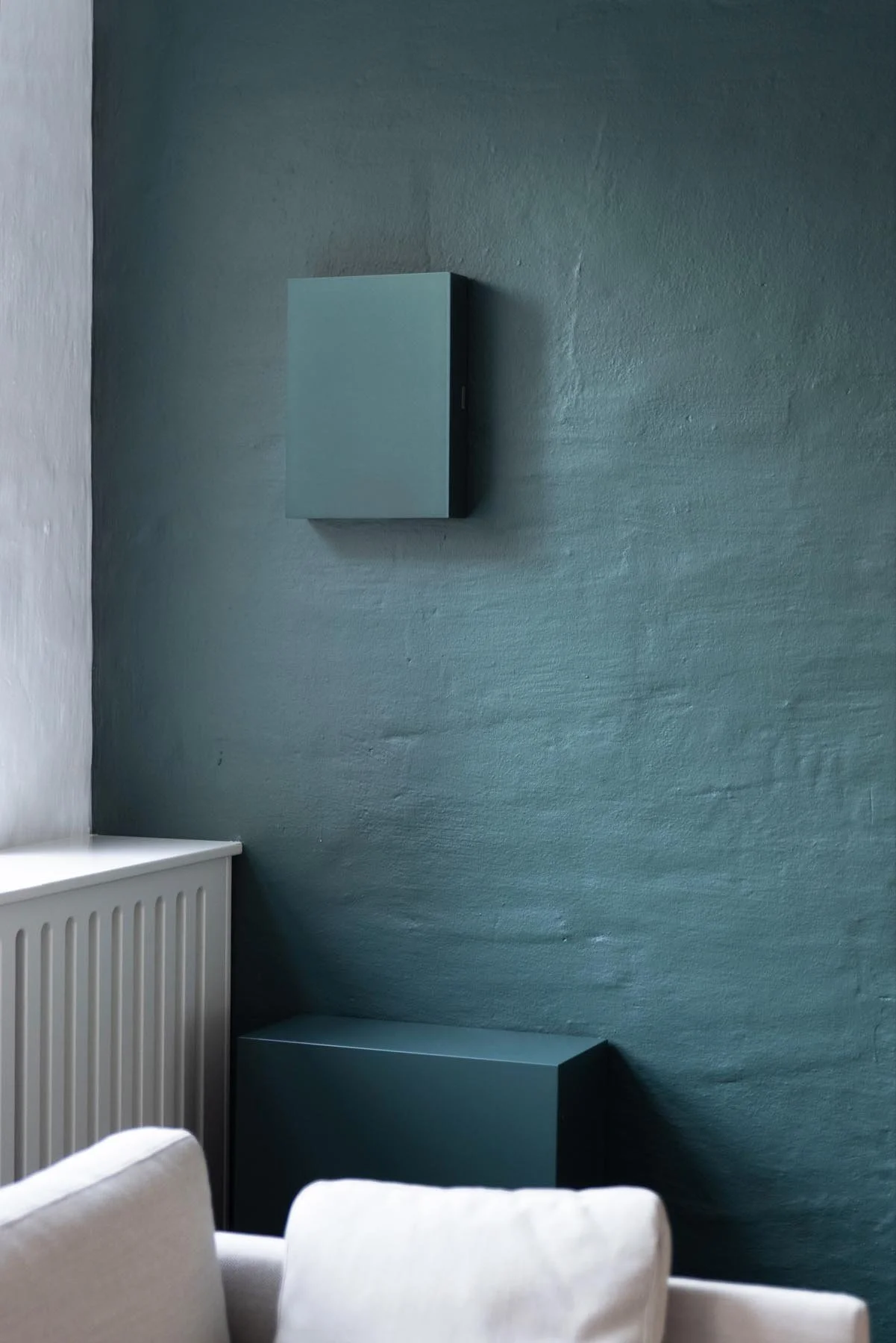 Blaue Wand mit zwei blauen Wandkästen, weißer Radiator und Teile eines weißen Sofas.