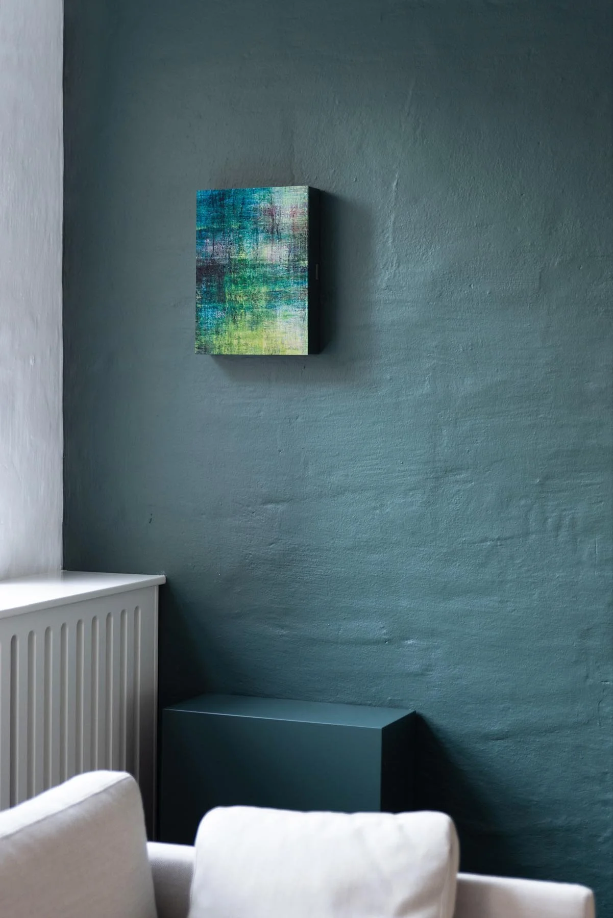 Gemütliches Wohnzimmer mit dunklem Wand, einem kleinen abstrakten Gemälde und weißen Möbeln.