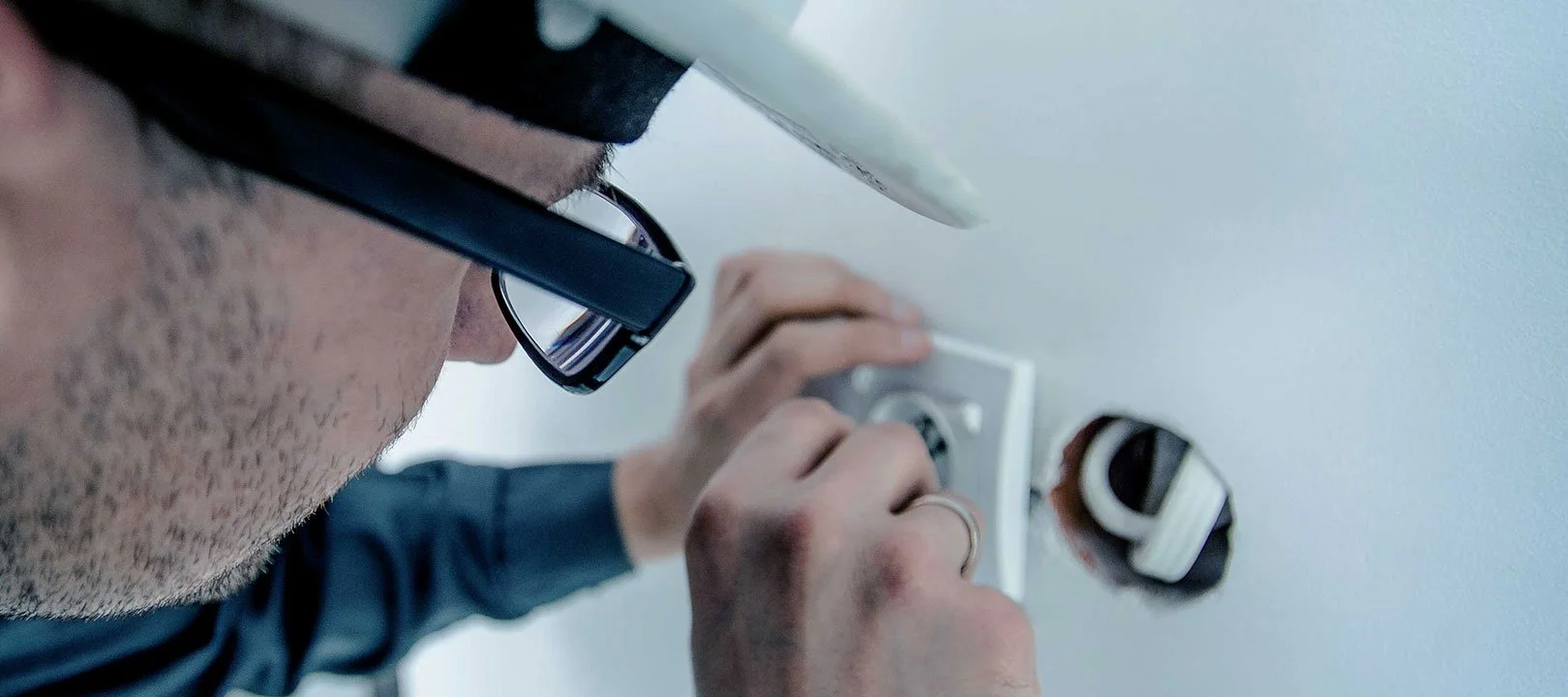 Ein Mann mit Brille arbeitet an einer Steckdose und installiert einen elektrischen Anschluss.
