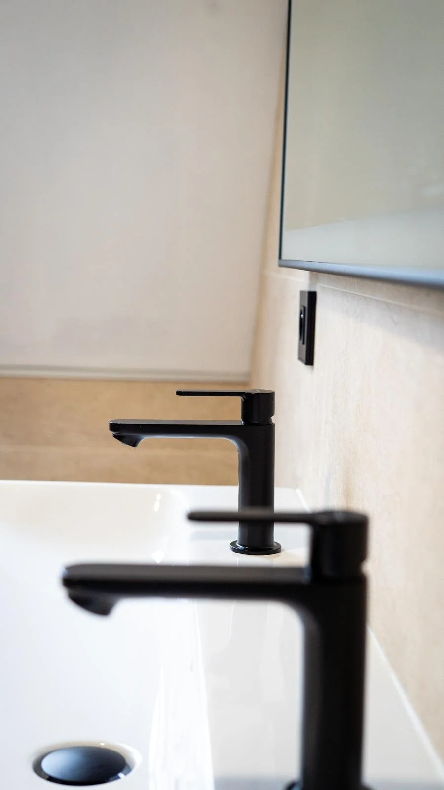 Trois robinets noirs au-dessus de lavabos dans une salle de bain, avec un miroir partiel à l'arrière-plans.