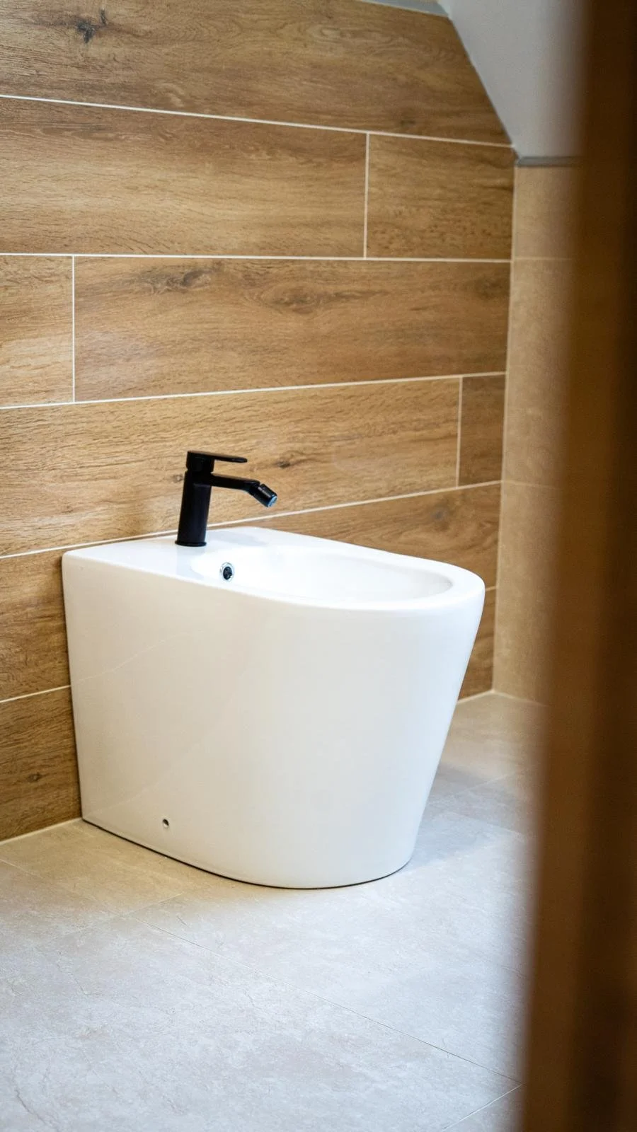 Un urinoir blanc avec un robinet noir fixé au mur en carrelage marron clair.