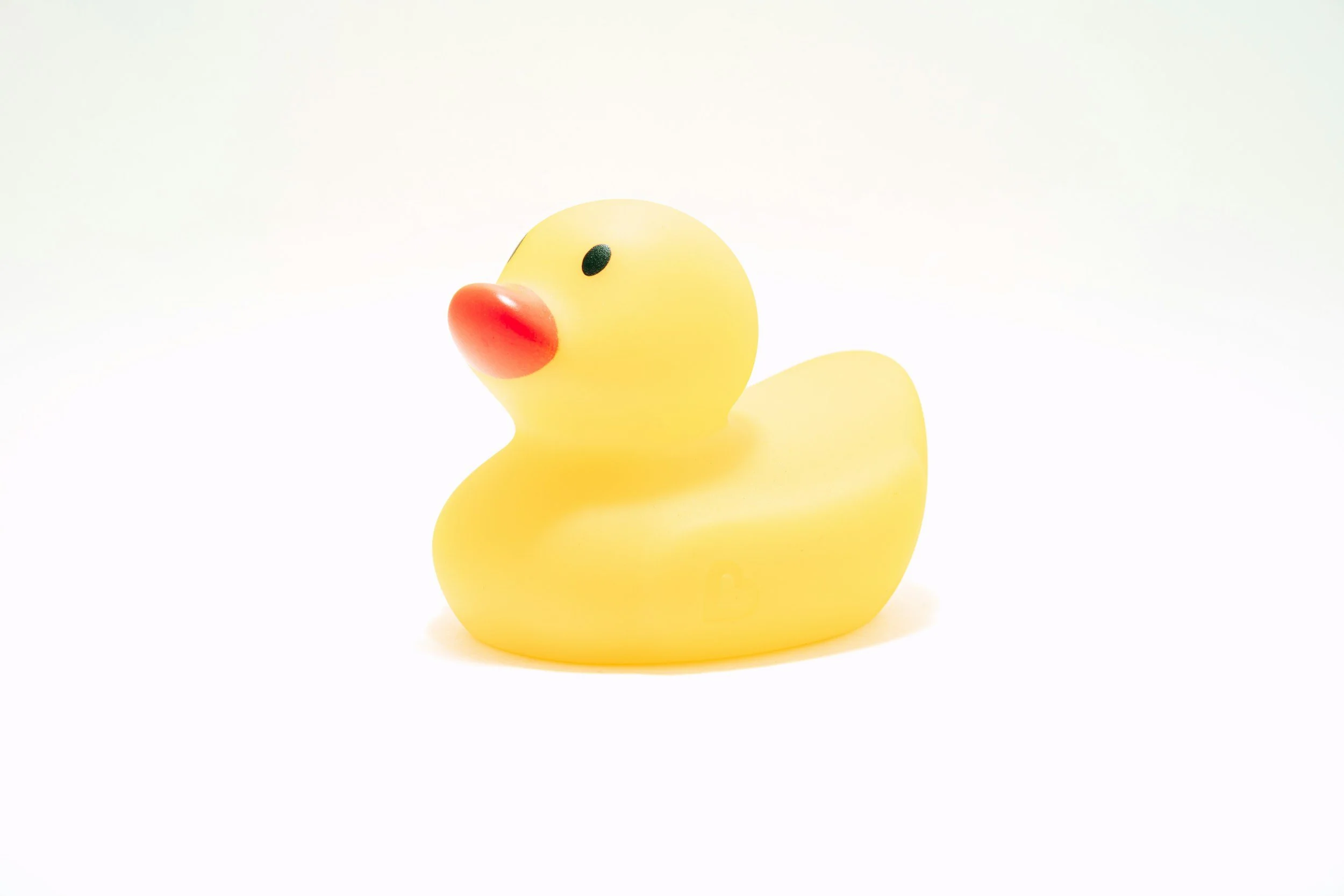 Yellow rubber duck with orange beak and black eyes on a white background.