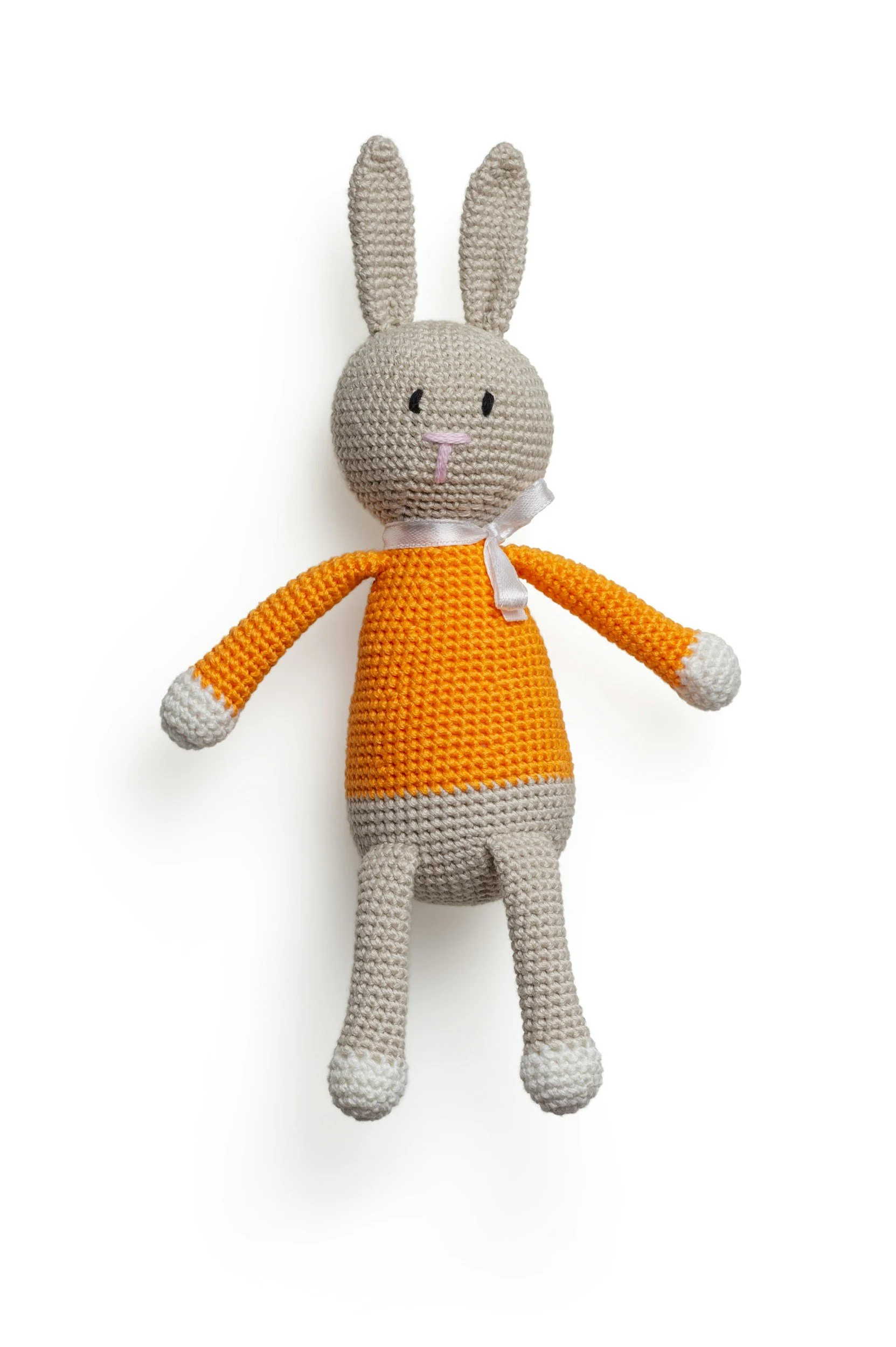 Handmade crocheted plush bunny toy with long ears, a gray face, pink nose, orange dress, white and gray striped legs, and a white bow around its neck on a white background.