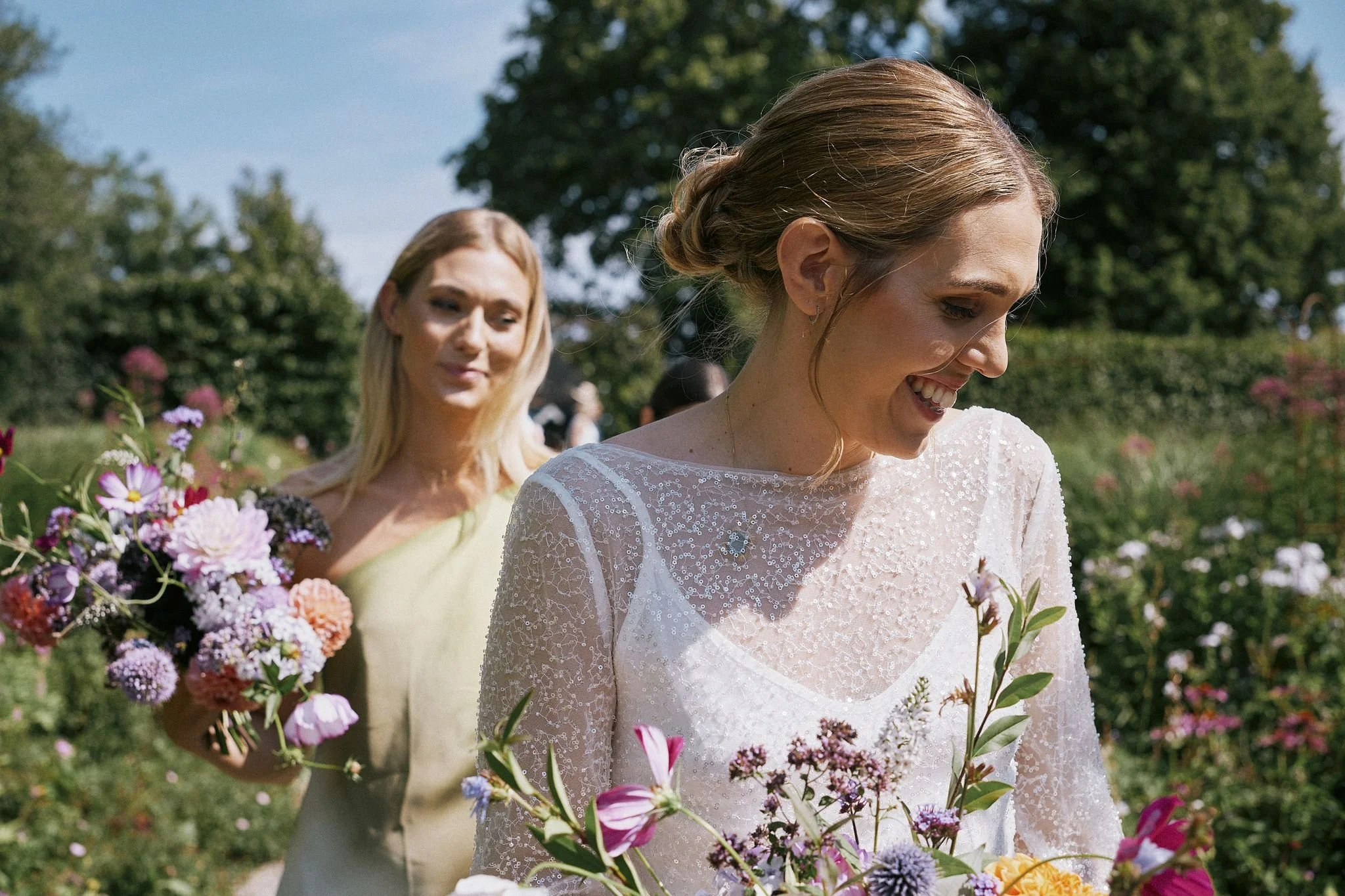 Brud med bukett går genom en trädgård på Österlen under bröllopsdagen
