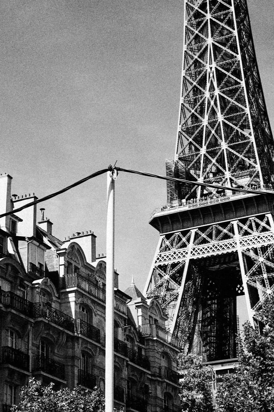 Svartvit bild av Eiffeltornet i Paris med omgivande byggnader och en gatlampor i förgrunden.